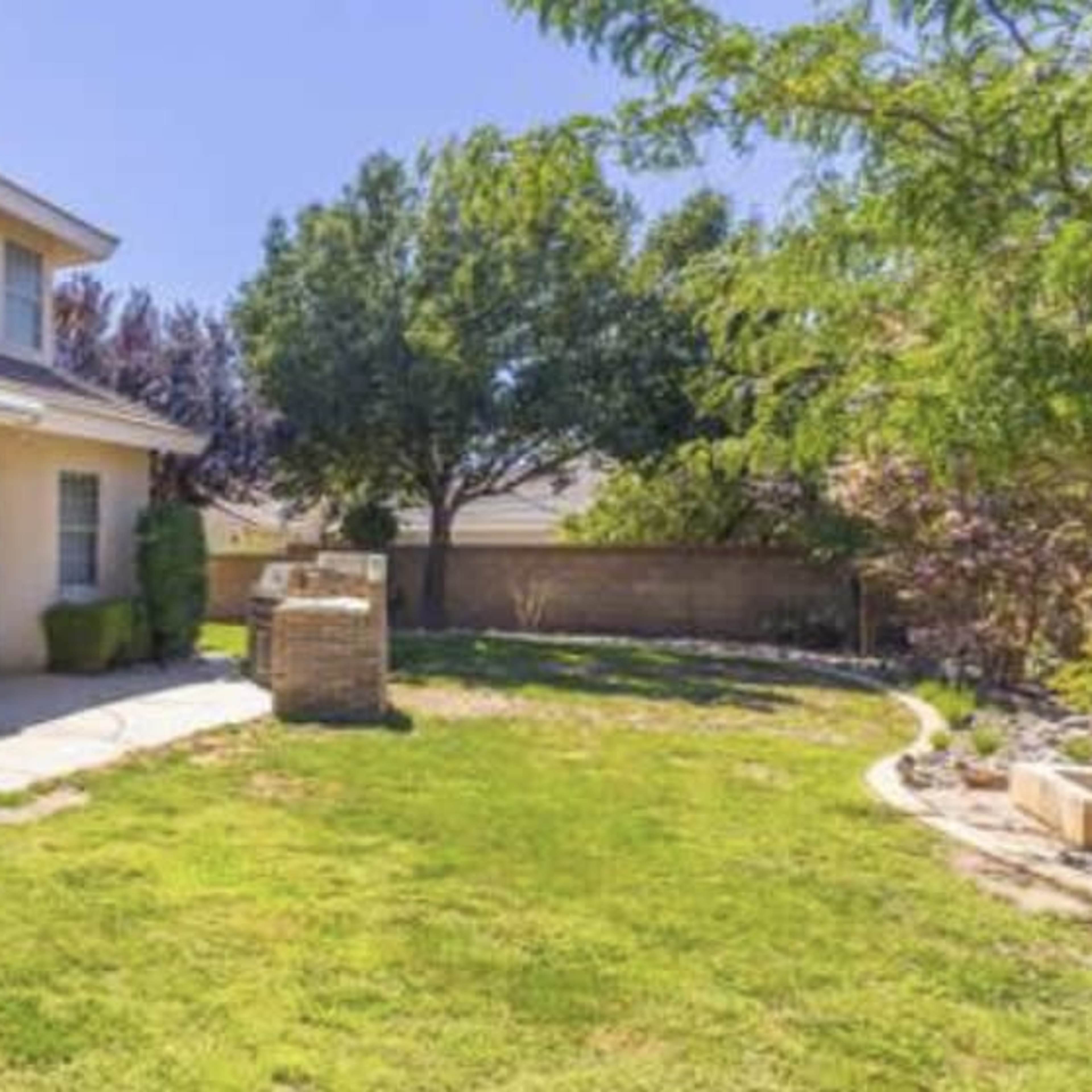 A two-story house with a front porch overlooks a grassy yard surrounded by trees and shrubs.