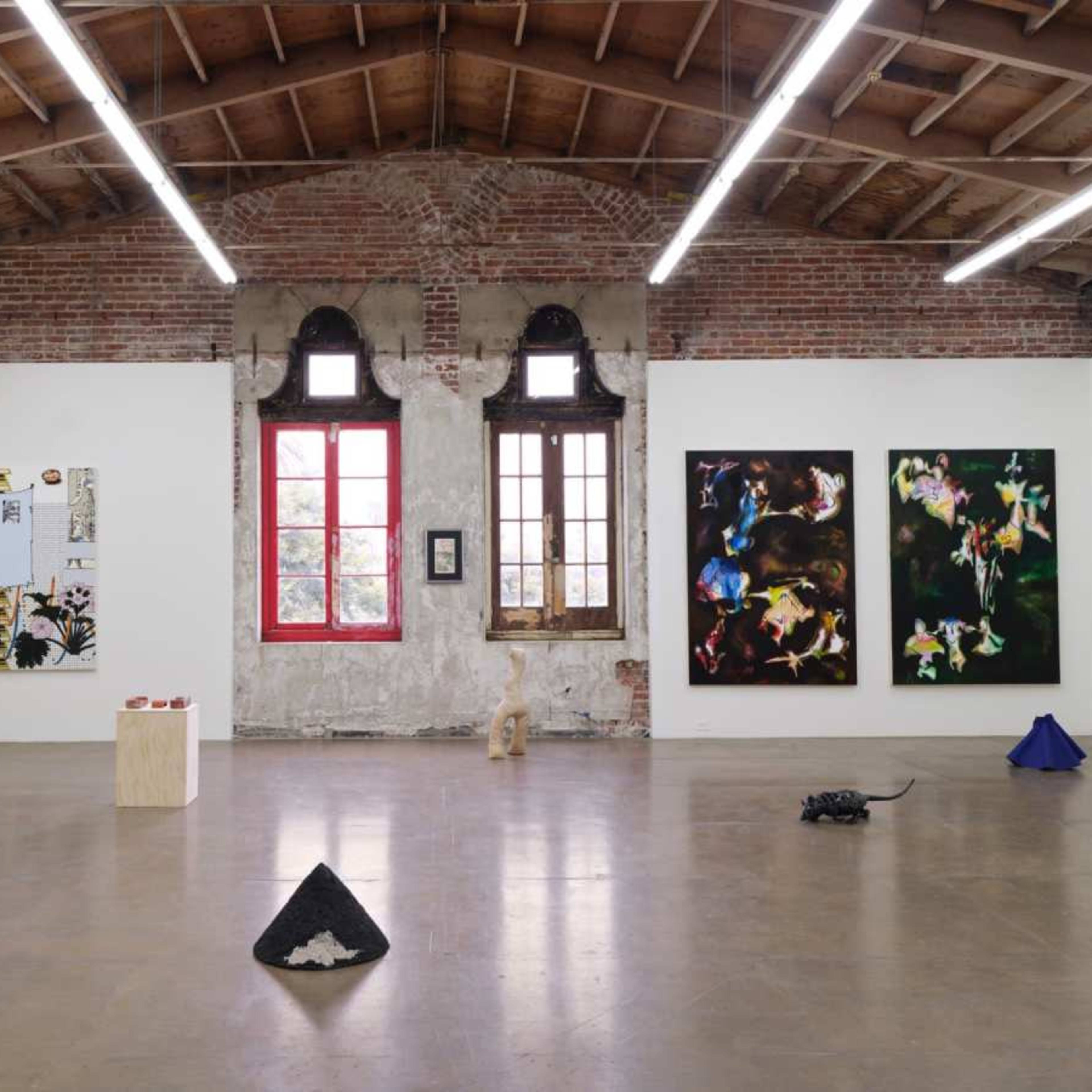 An art gallery featuring various artworks displayed on white walls, with brick accents and large windows.
