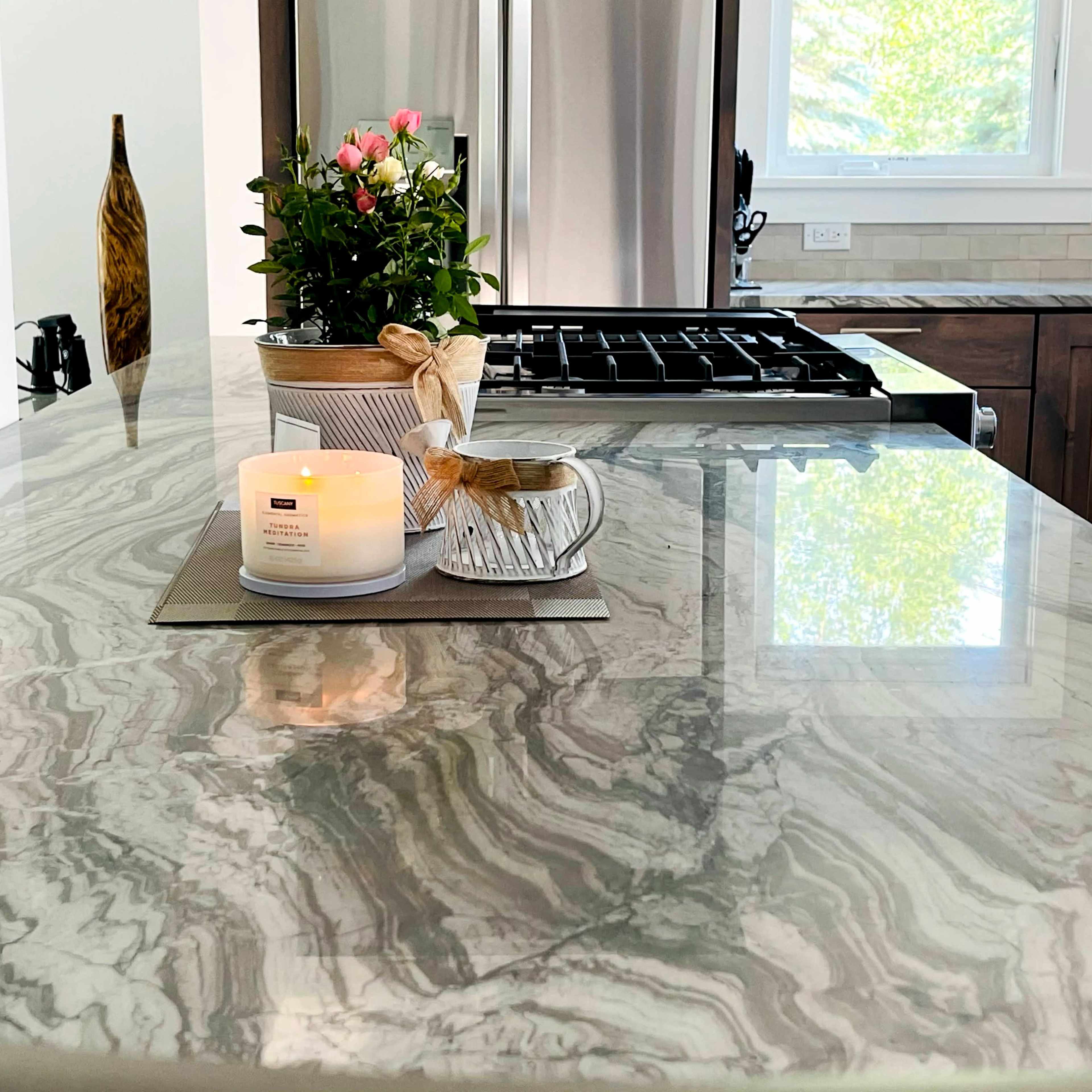 A marble kitchen countertop is adorned with a candle, a small potted plant, and a decorative dish, all near the appliance area.