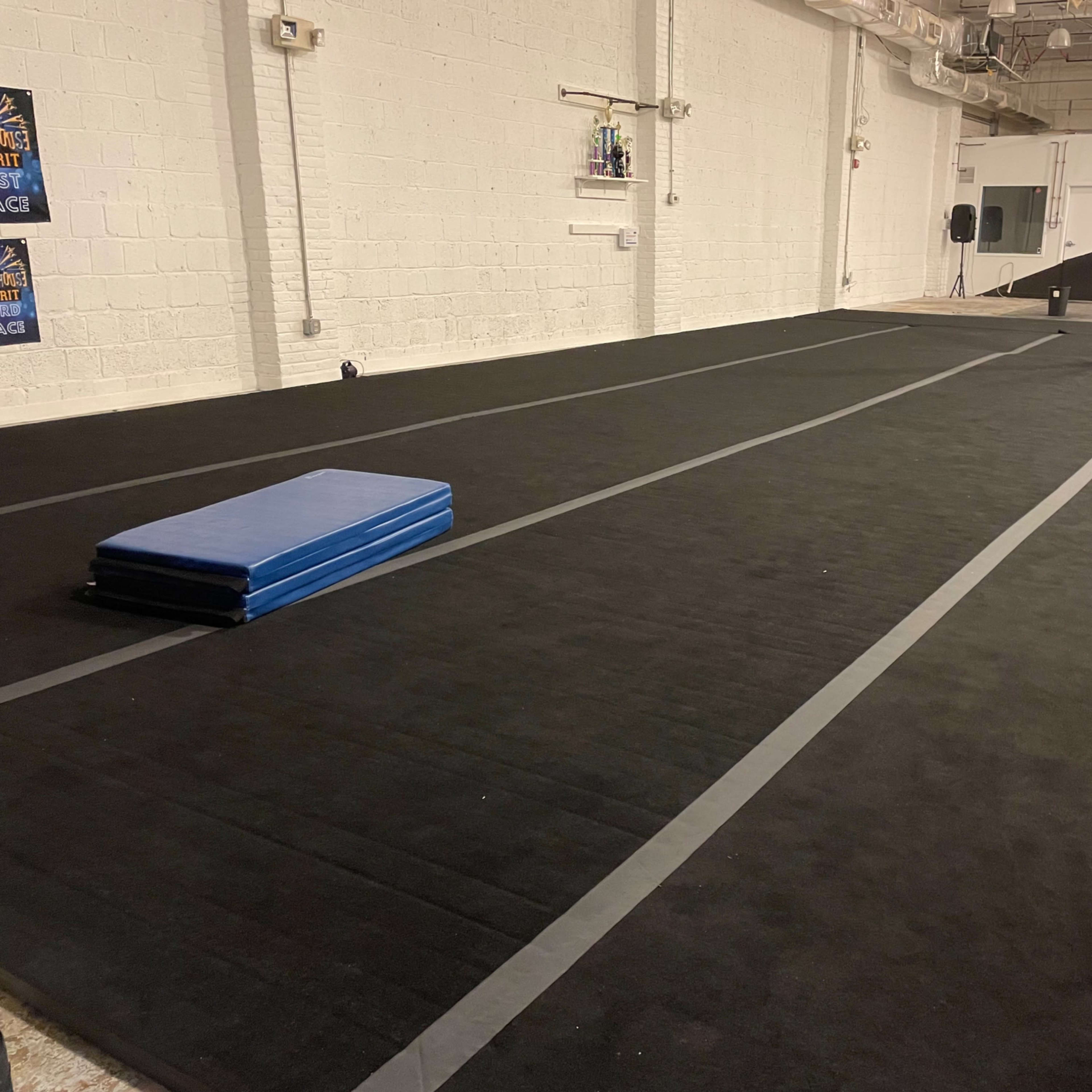 A spacious gymnasium floor with black rubber flooring and a blue gym mat placed on it.