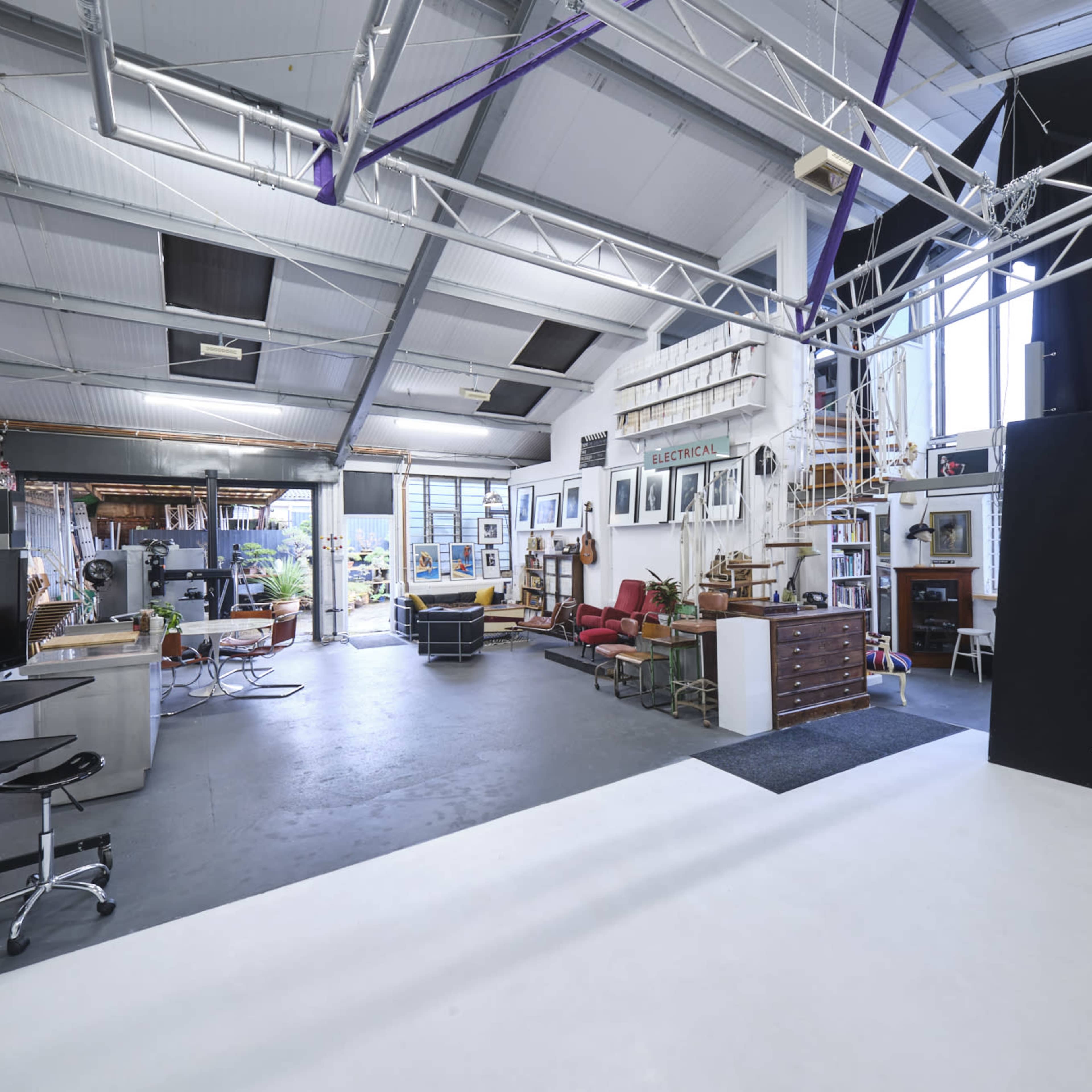 A spacious studio with various workstations, large windows allowing natural light, and eclectic furnishings arranged around the area.