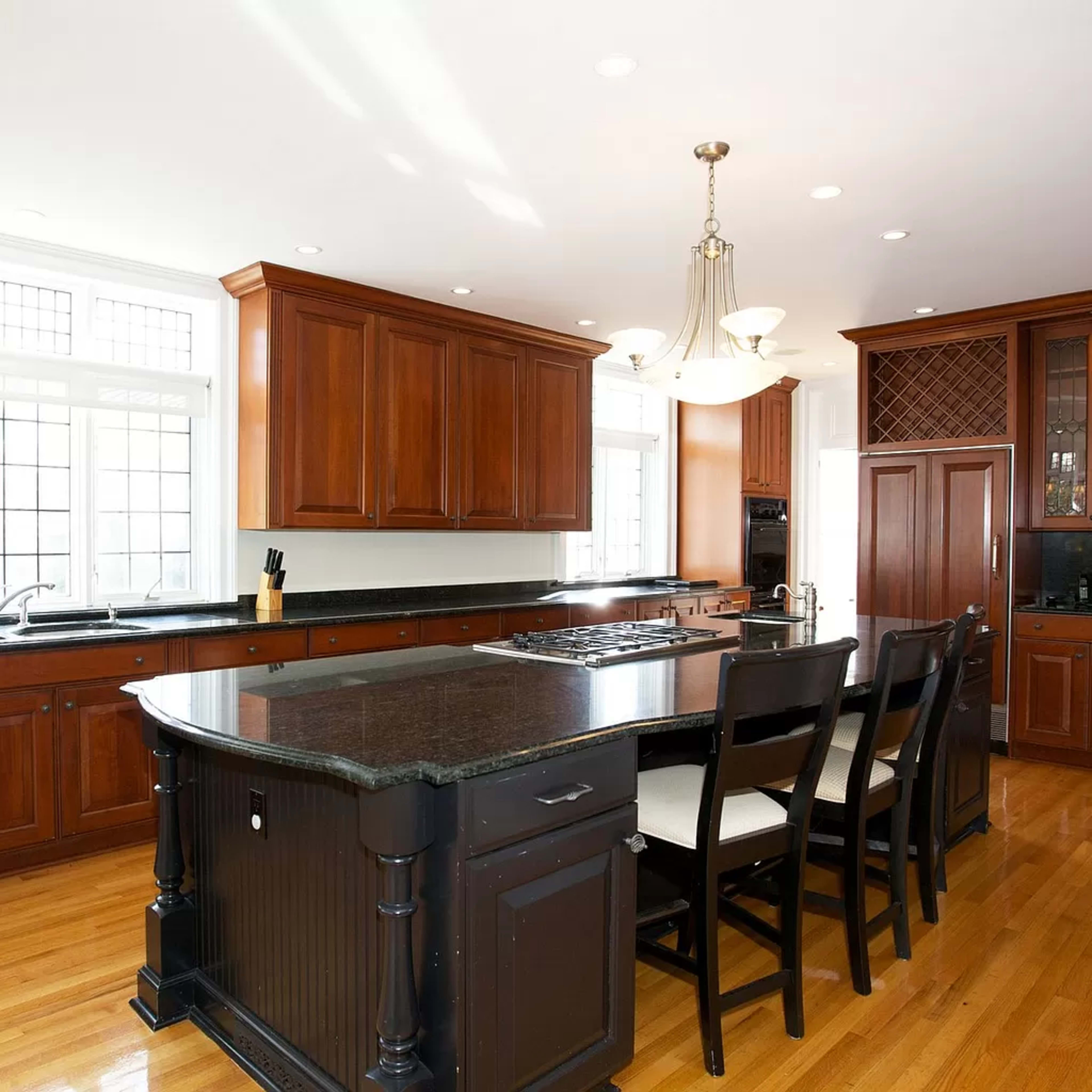 A large kitchen featuring dark wood cabinets, a black countertop island with seating, and multiple windows providing natural light.