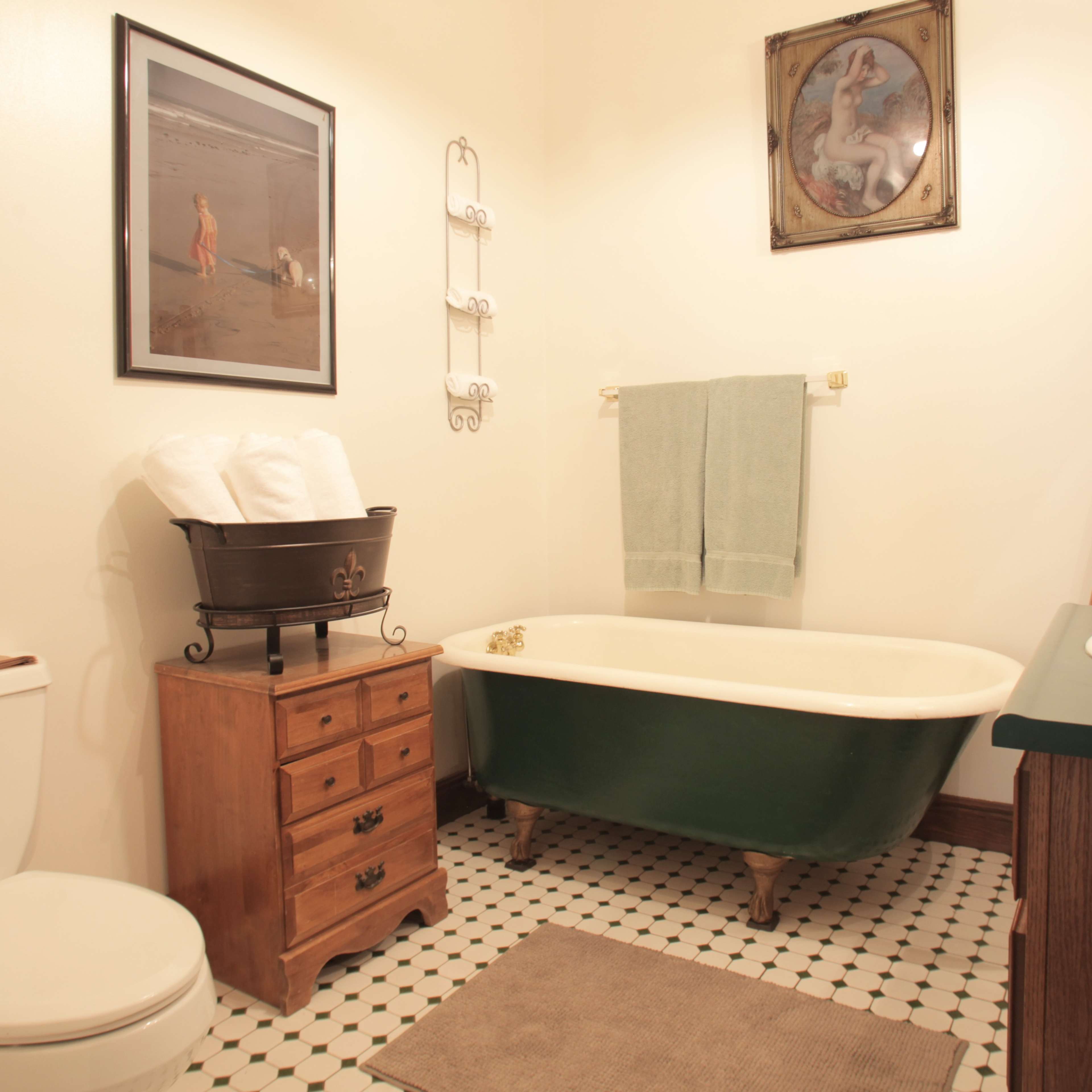 A bathroom featuring a green clawfoot tub, a wooden side table, a sink with a dark countertop, and decorative items on a ladder shelf.