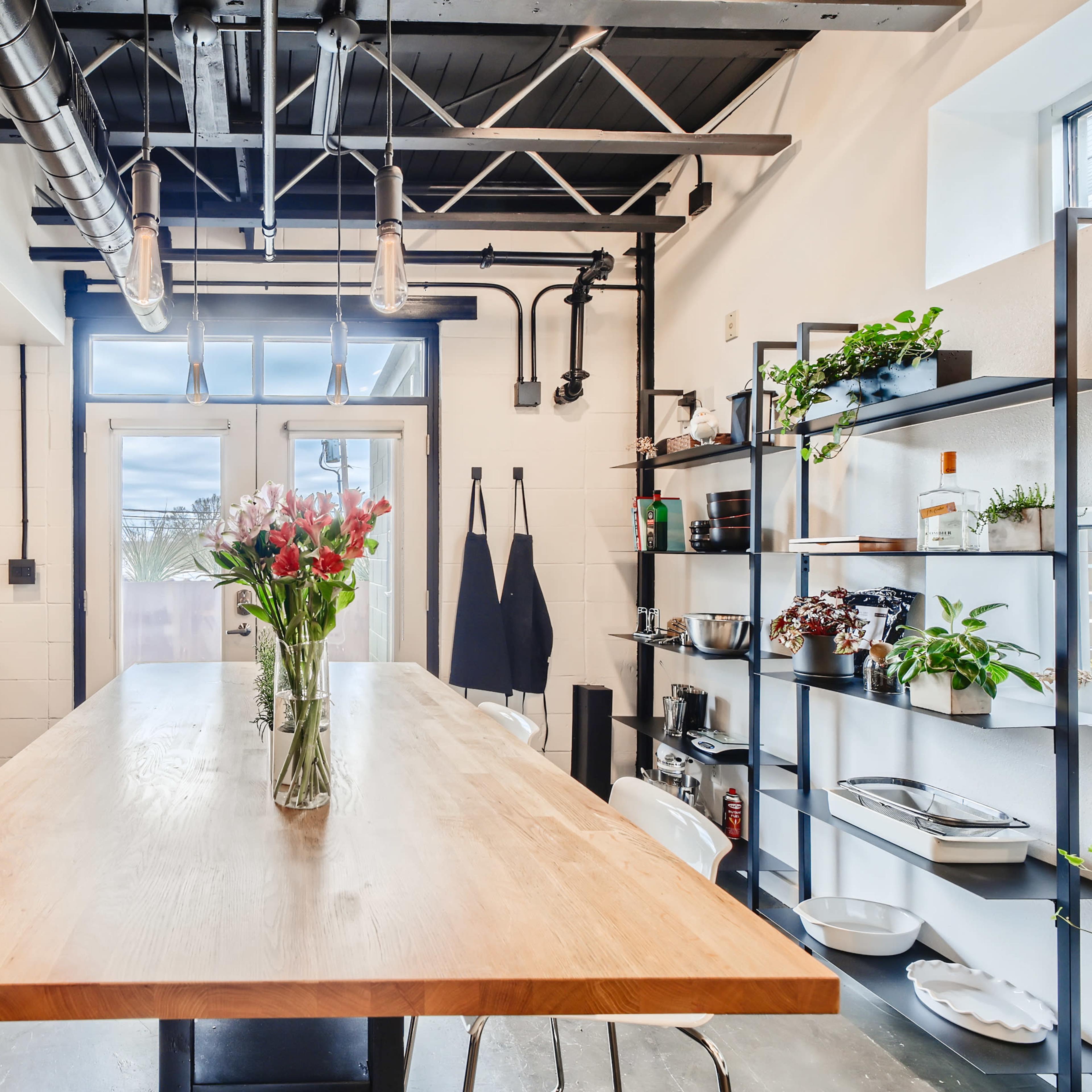 A modern kitchen features black cabinetry, stainless steel appliances, and a large wooden island with a vase of flowers.