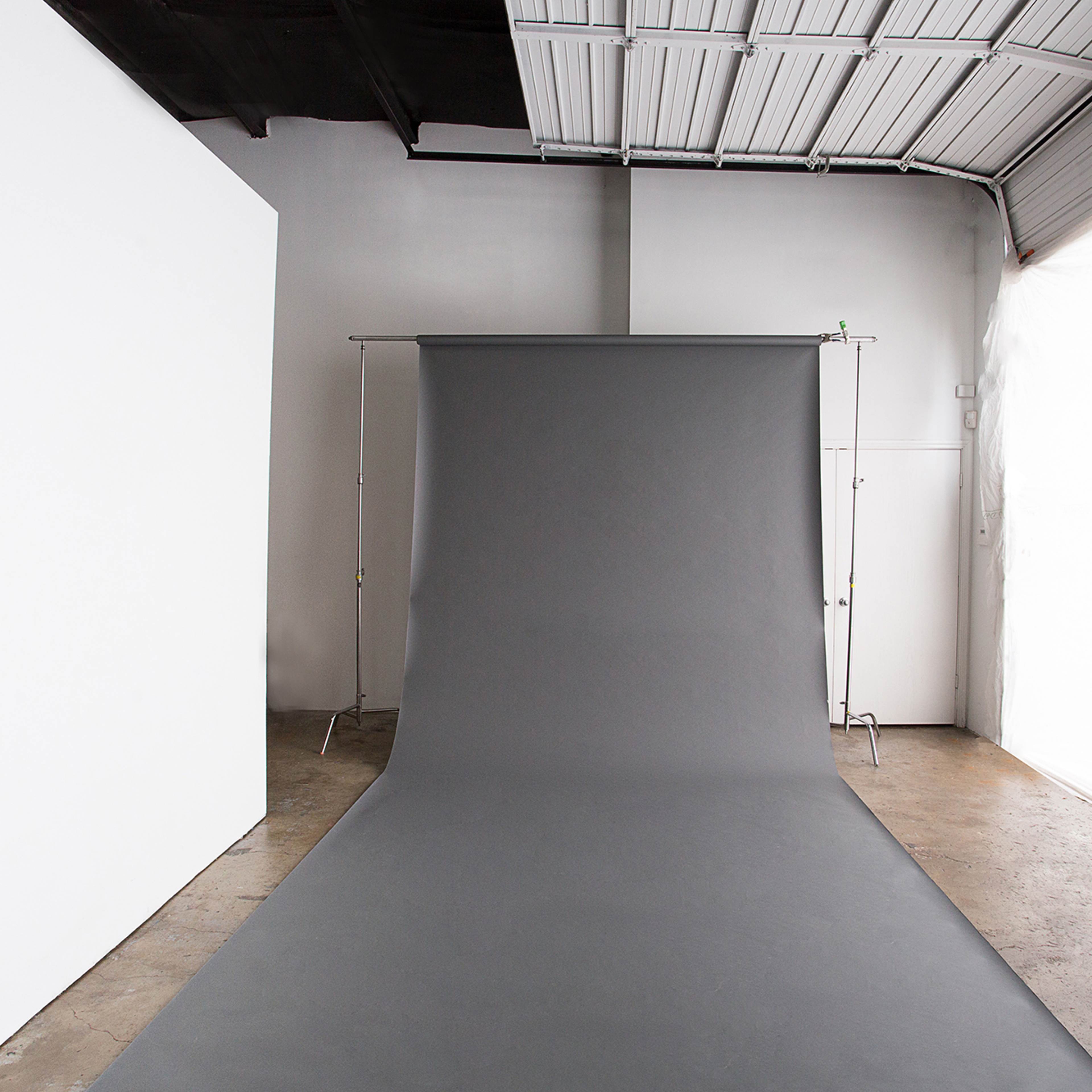 A photography studio with a gray backdrop on a seamless roll and a white wall to the left.