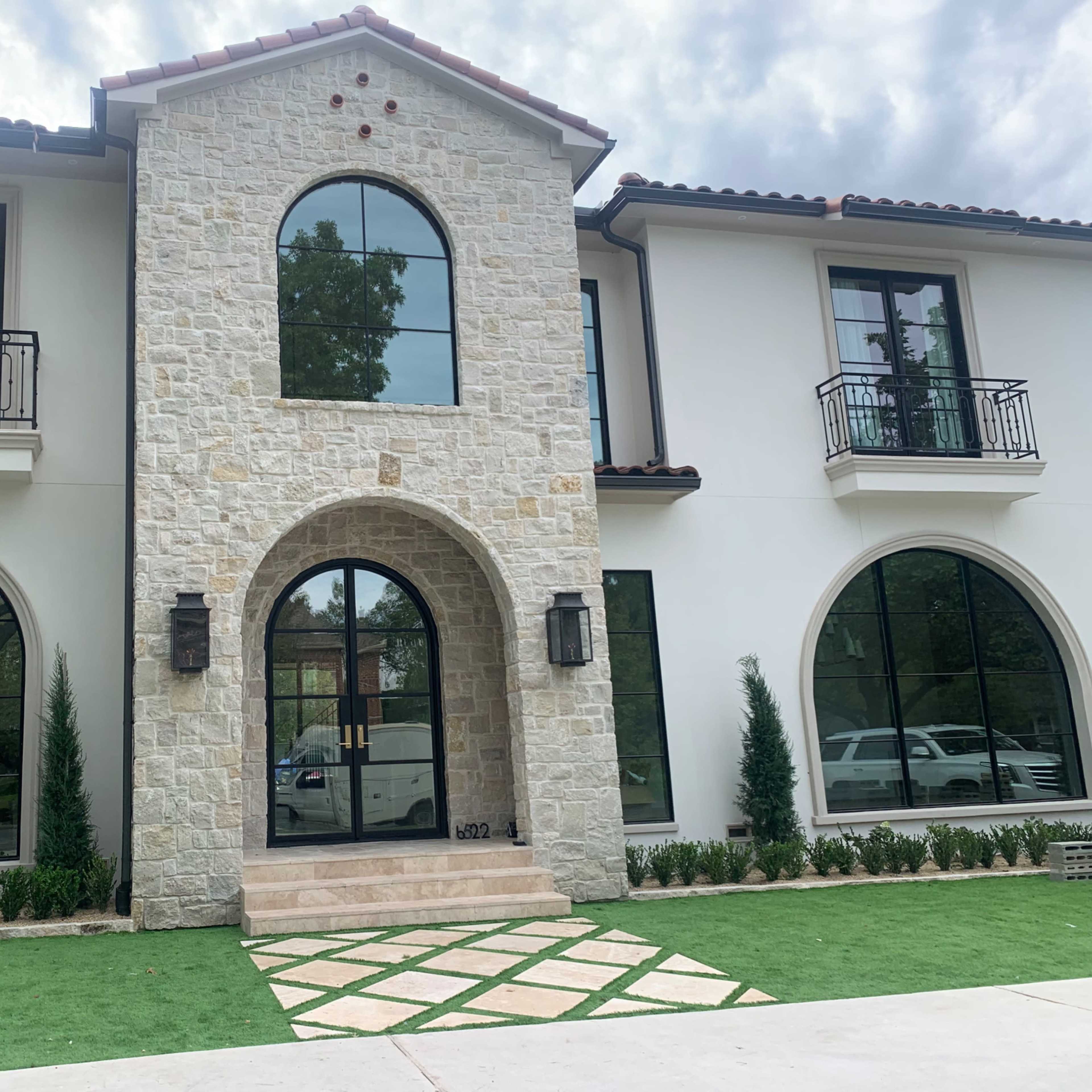 A two-story house featuring a stone facade, large arched windows, and a central arched entrance.