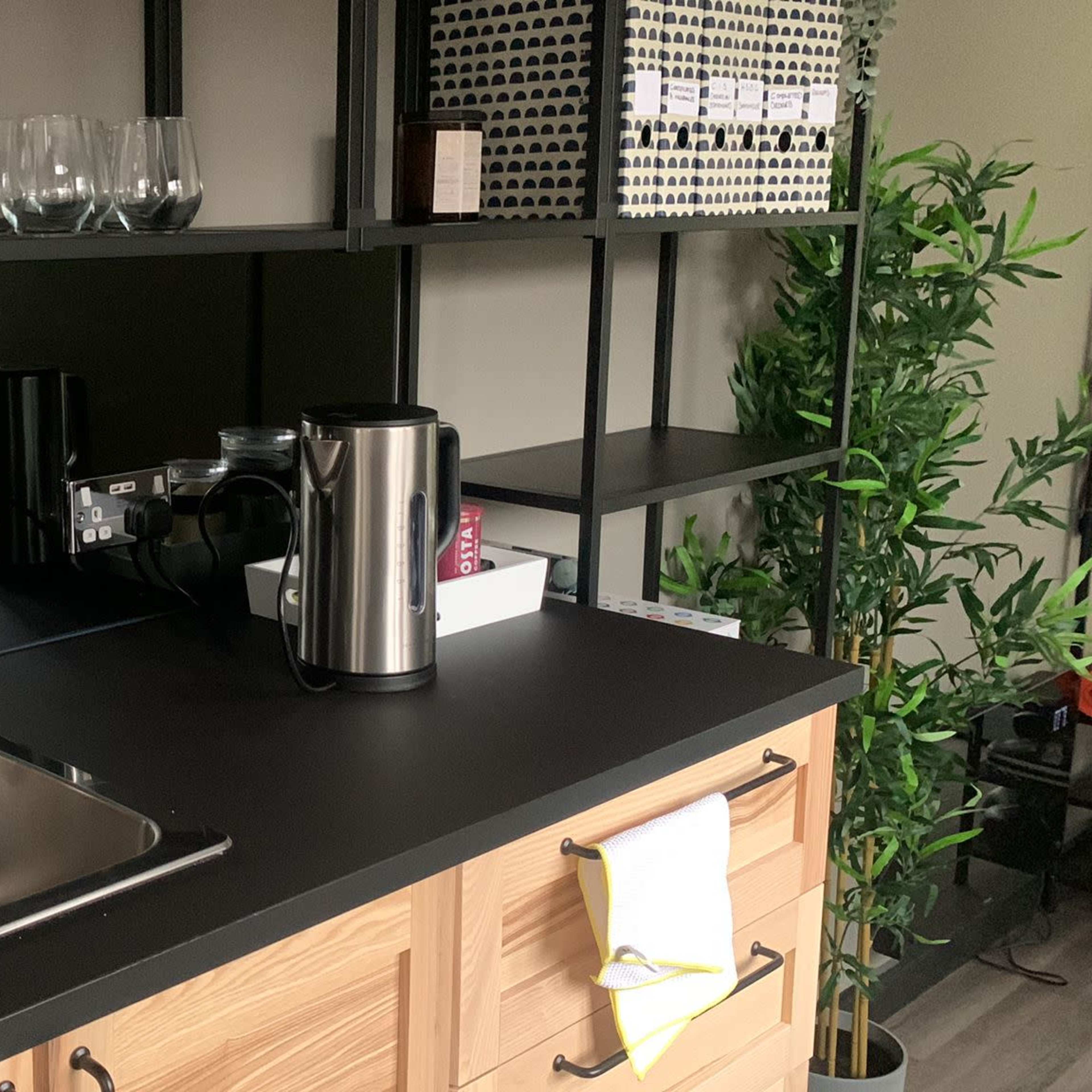 A modern kitchen countertop with a stainless steel sink, a kettle, and an assortment of cups and glasses on shelves above.