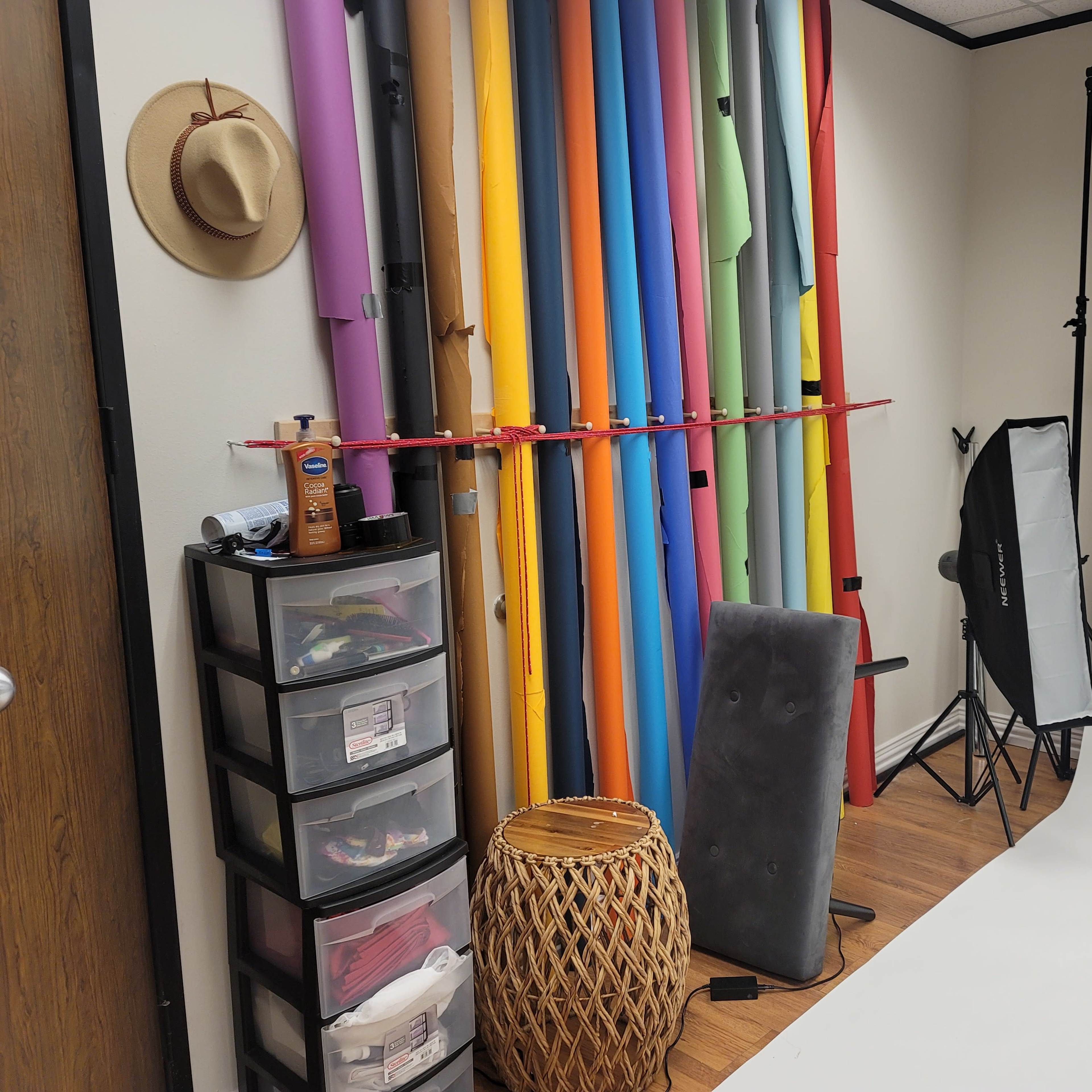 A photography studio with a backdrop of colorful rolls of paper, a storage unit, and lighting equipment.