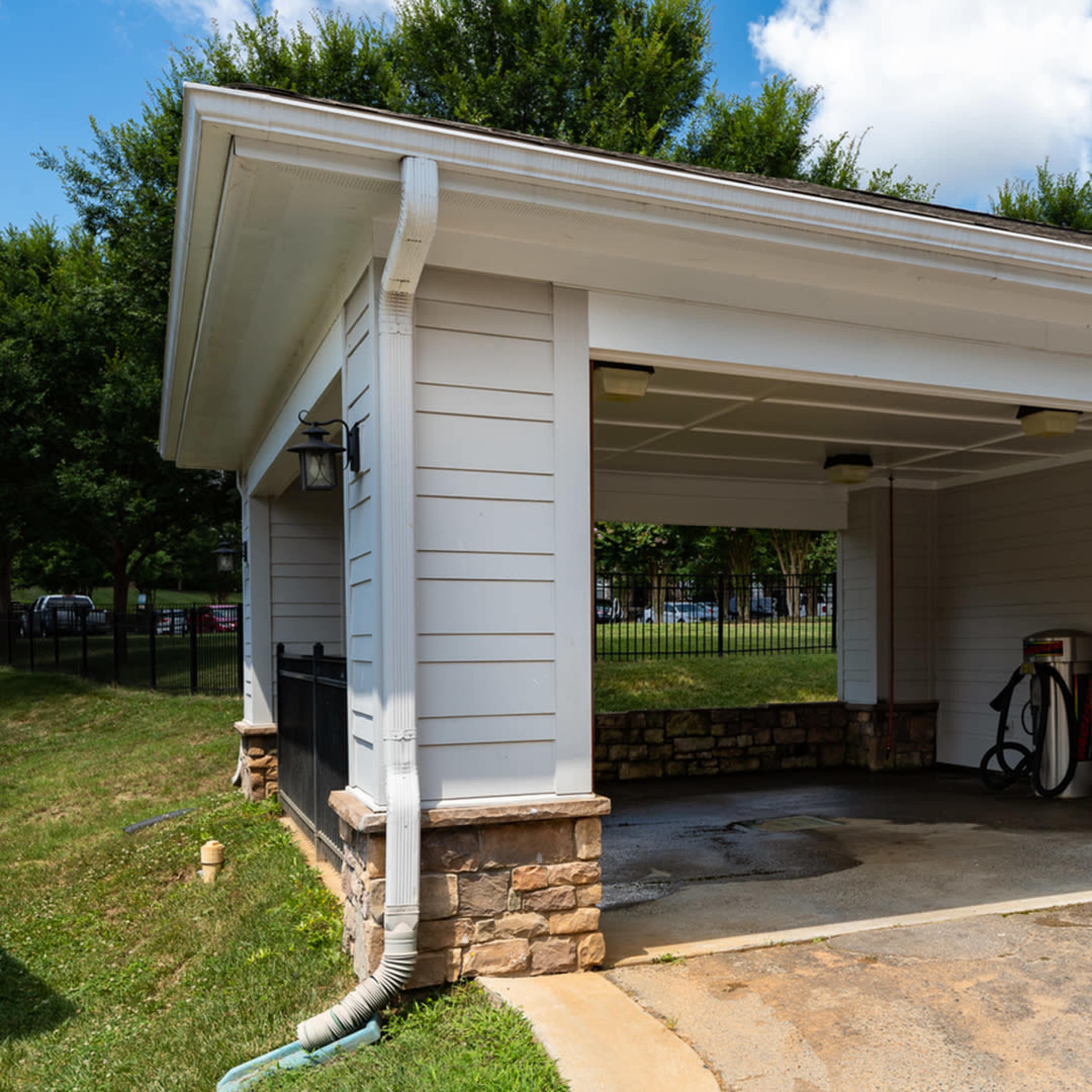 A two-car garage with a stone foundation and a fuel pump on the left side, surrounded by grass and trees.