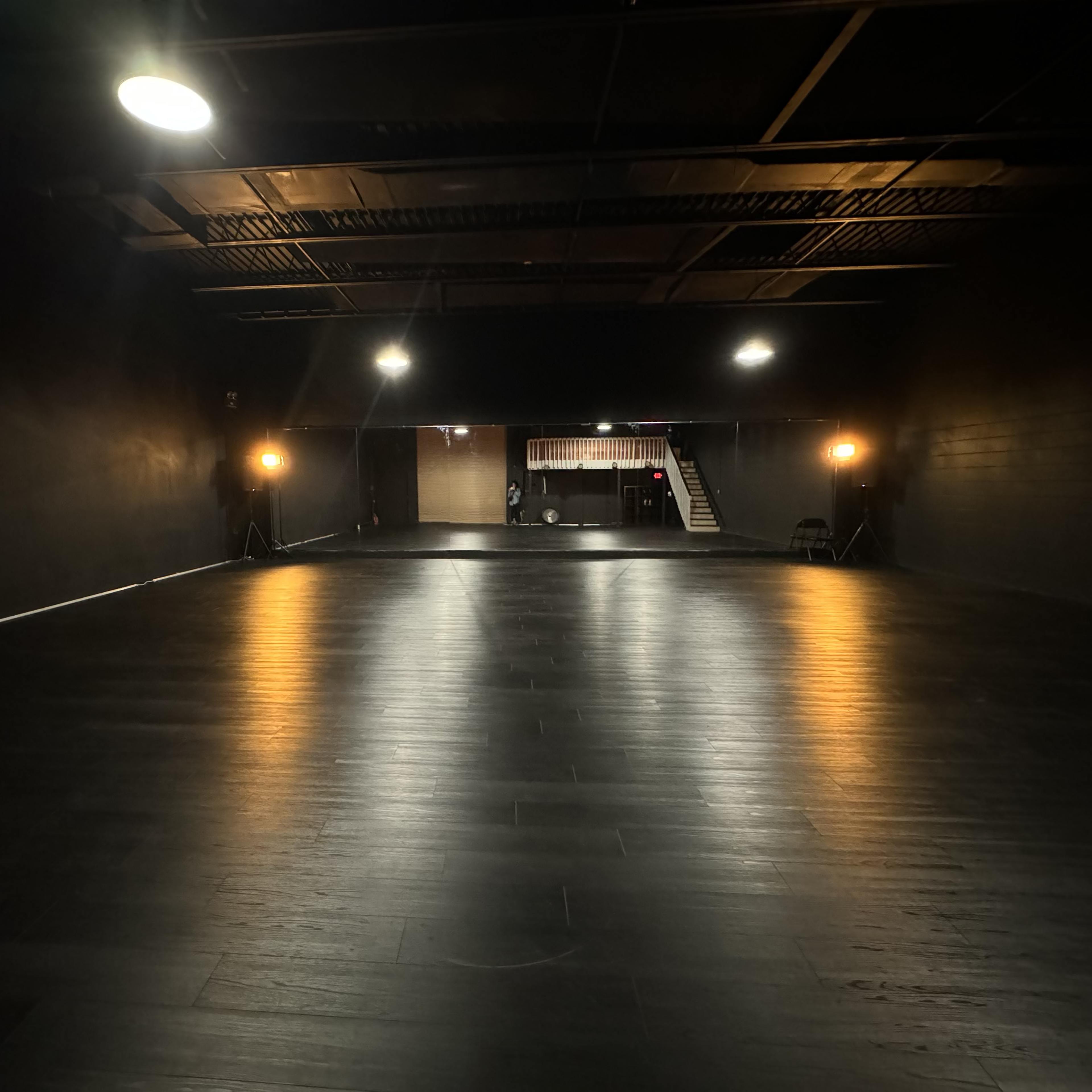 A large, empty, dimly lit studio space with black walls and a polished wooden floor.