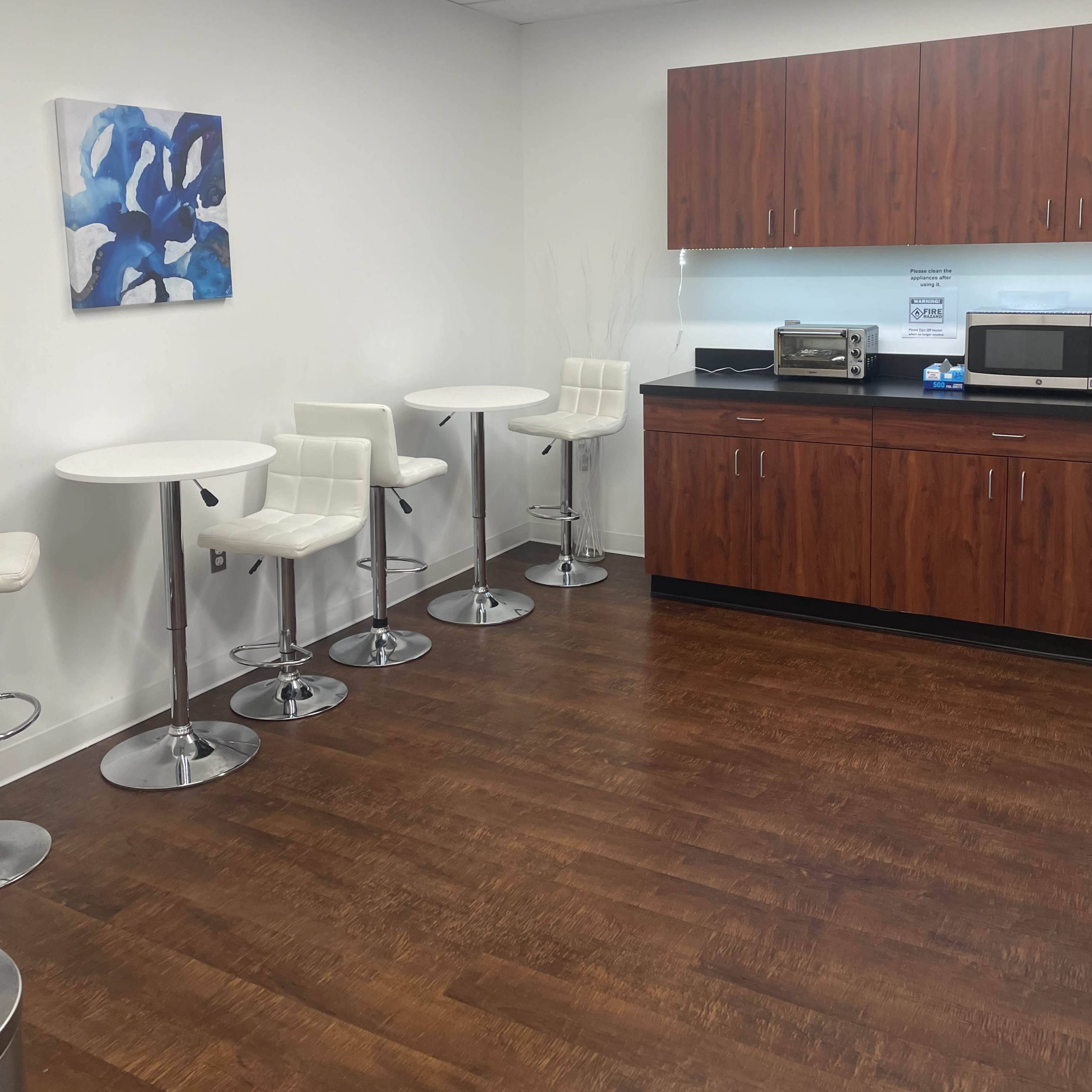 A break room with bar stools, small round tables, and a kitchen cabinet containing a microwave and other appliances.