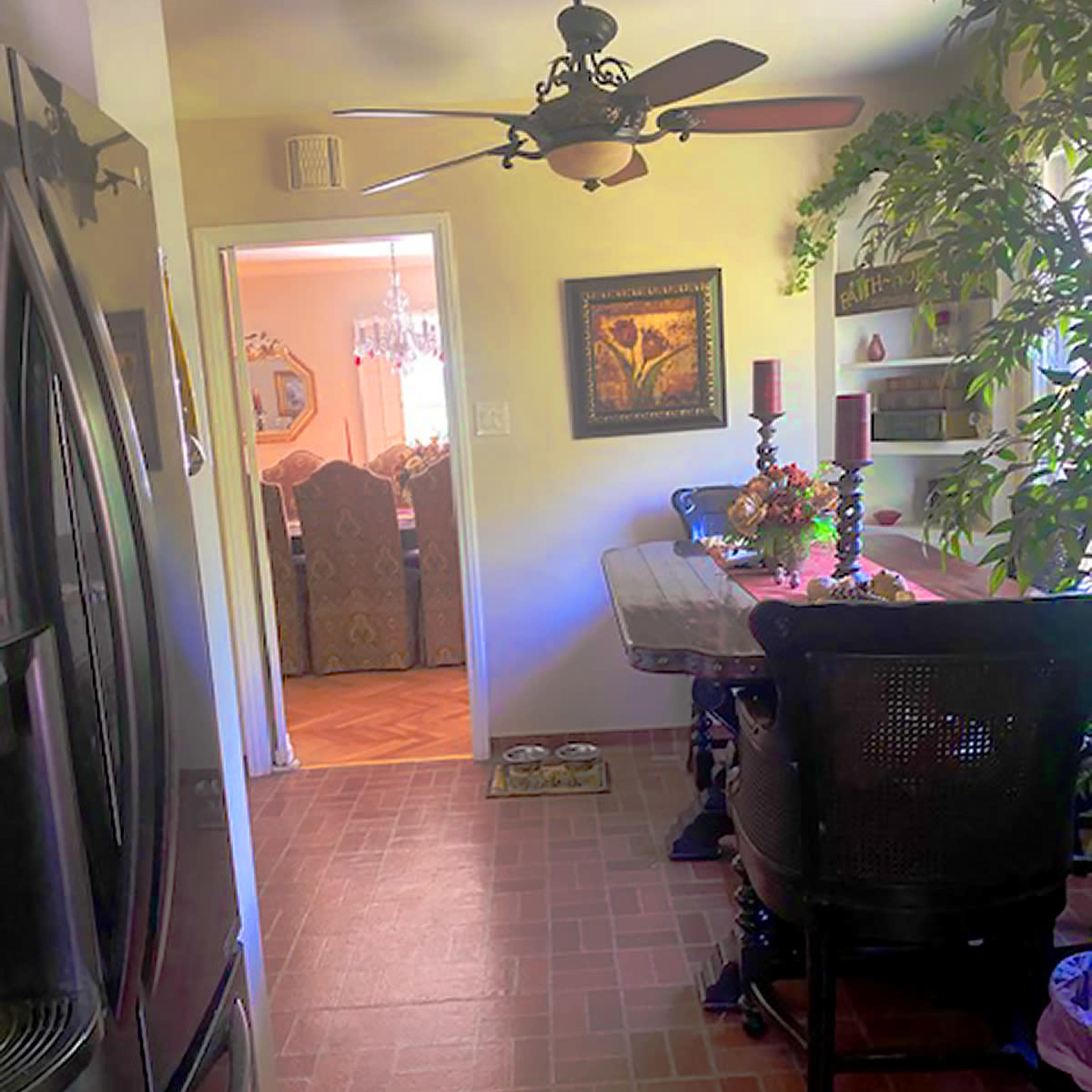 A dining area with a table and chairs is visible, adjacent to a kitchen, featuring a ceiling fan and decorative plants.