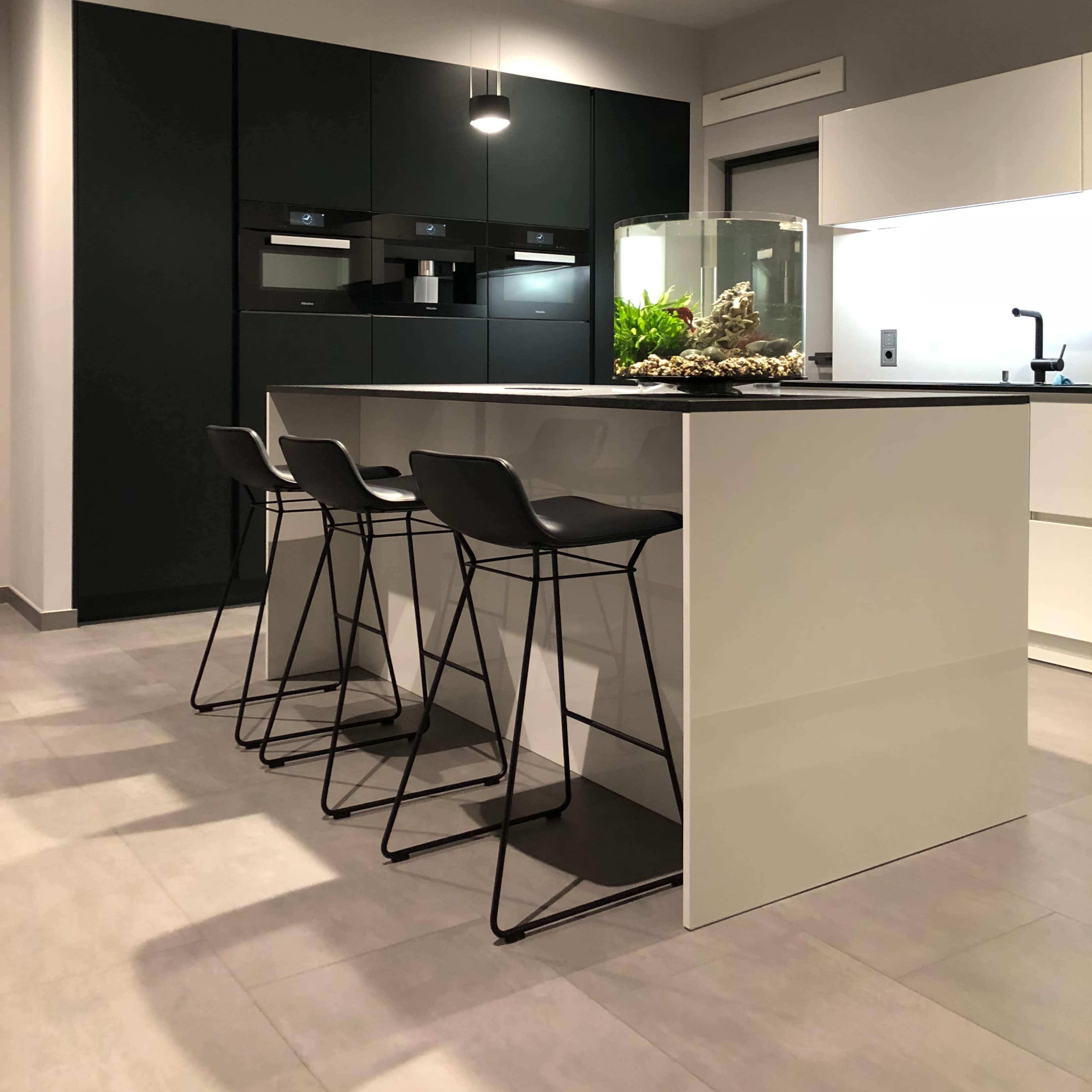 A modern kitchen features a central island with four black bar stools, surrounded by sleek cabinetry and pendant lighting.