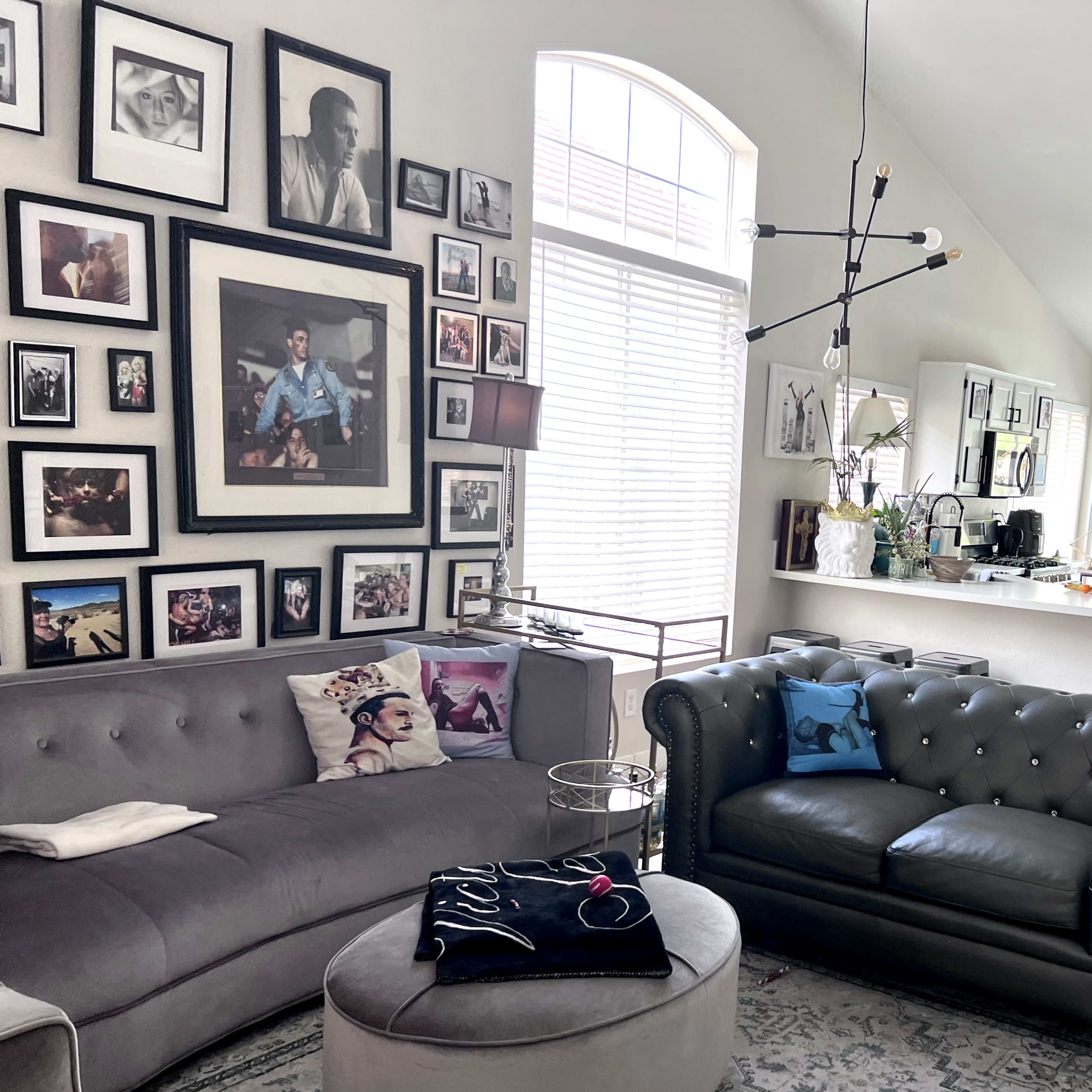 The living room features a gray sectional sofa and a black tufted armchair, surrounded by a gallery wall of framed photos and artwork, with a modern light fixture overhead.