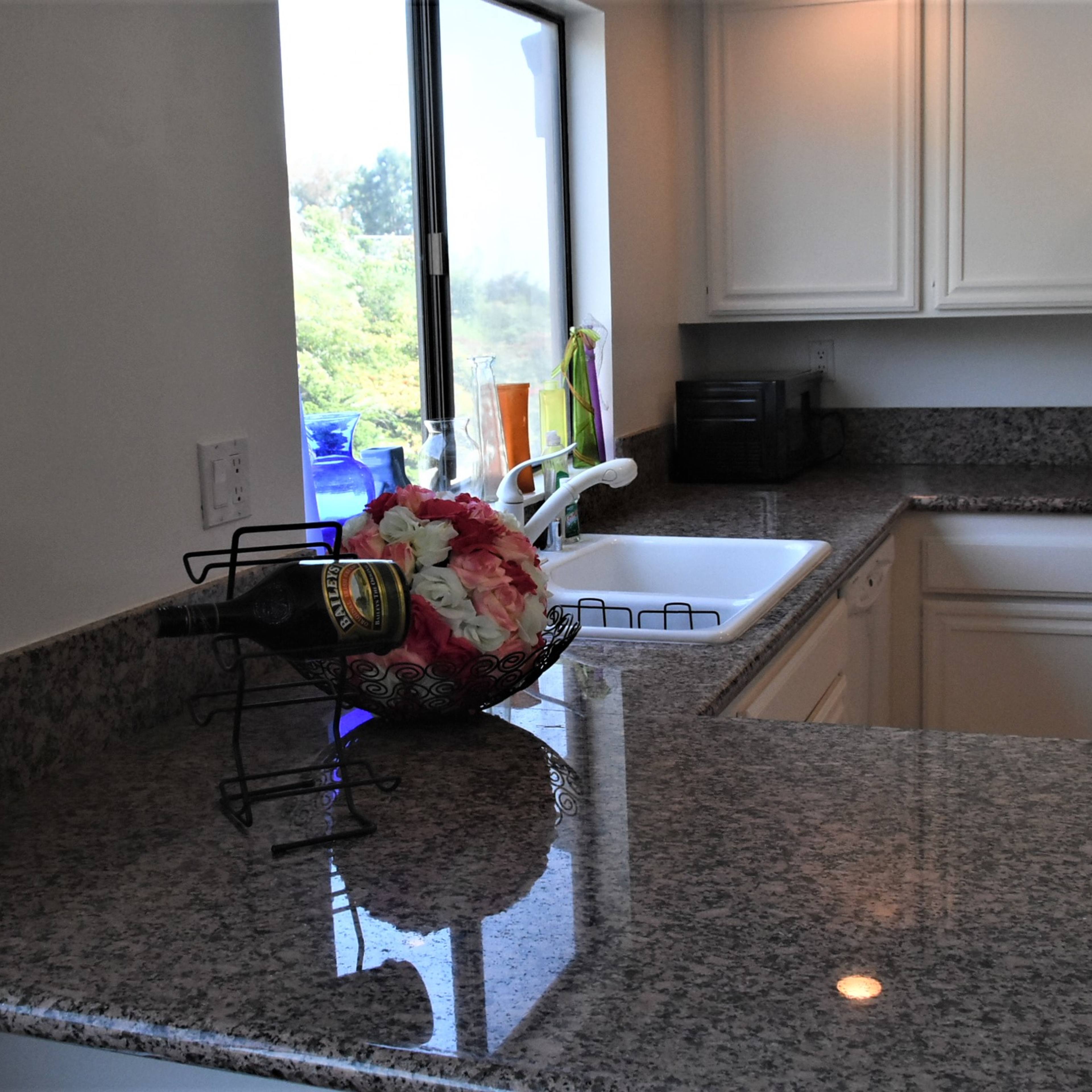 A kitchen features a granite countertop with a bouquet of flowers and a window overlooking greenery.