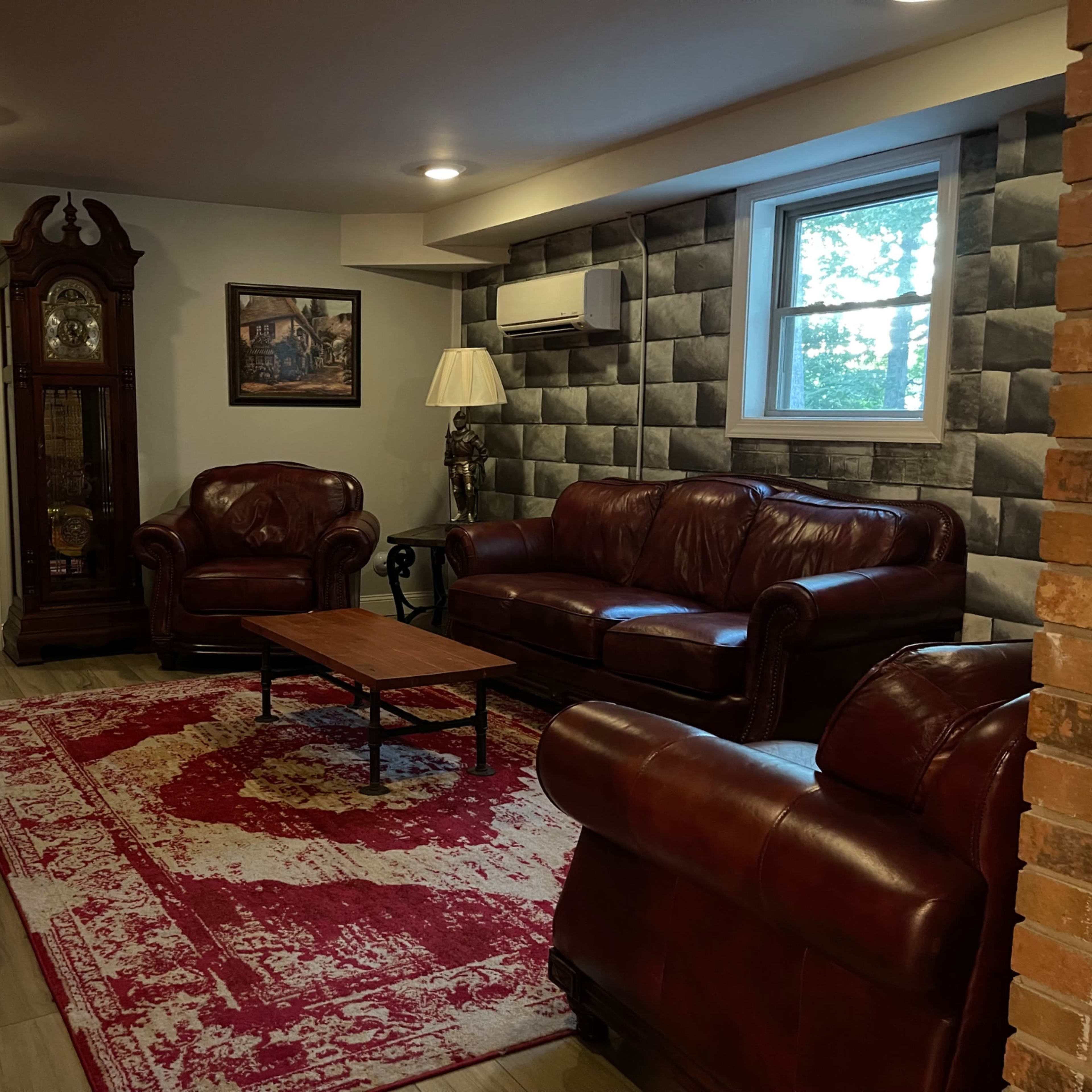 A living room with leather sofas, a wooden coffee table, a decorative rug, and a large wall clock against a backdrop of textured wallpaper.
