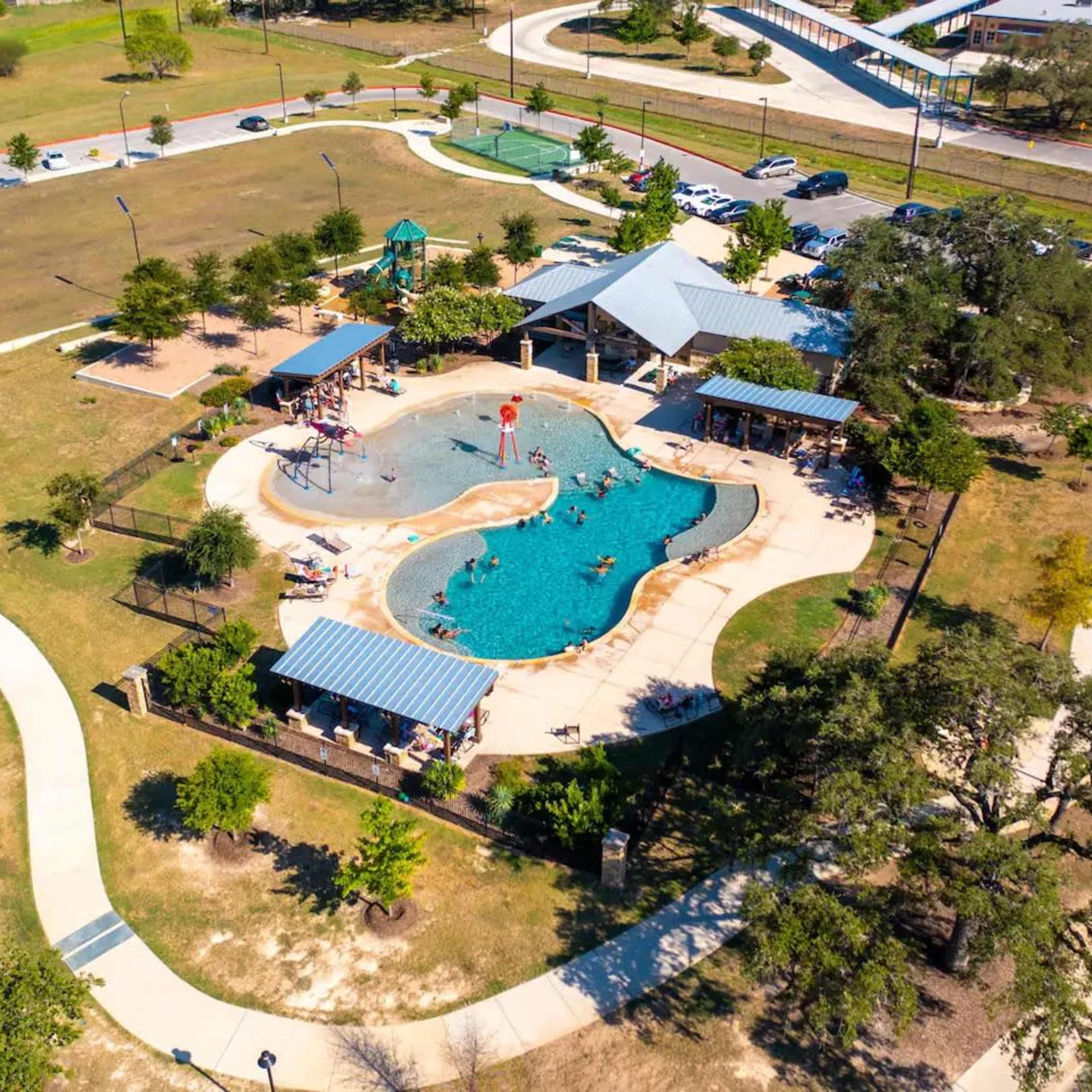 A community pool area surrounded by greenery, pathways, and recreational facilities.