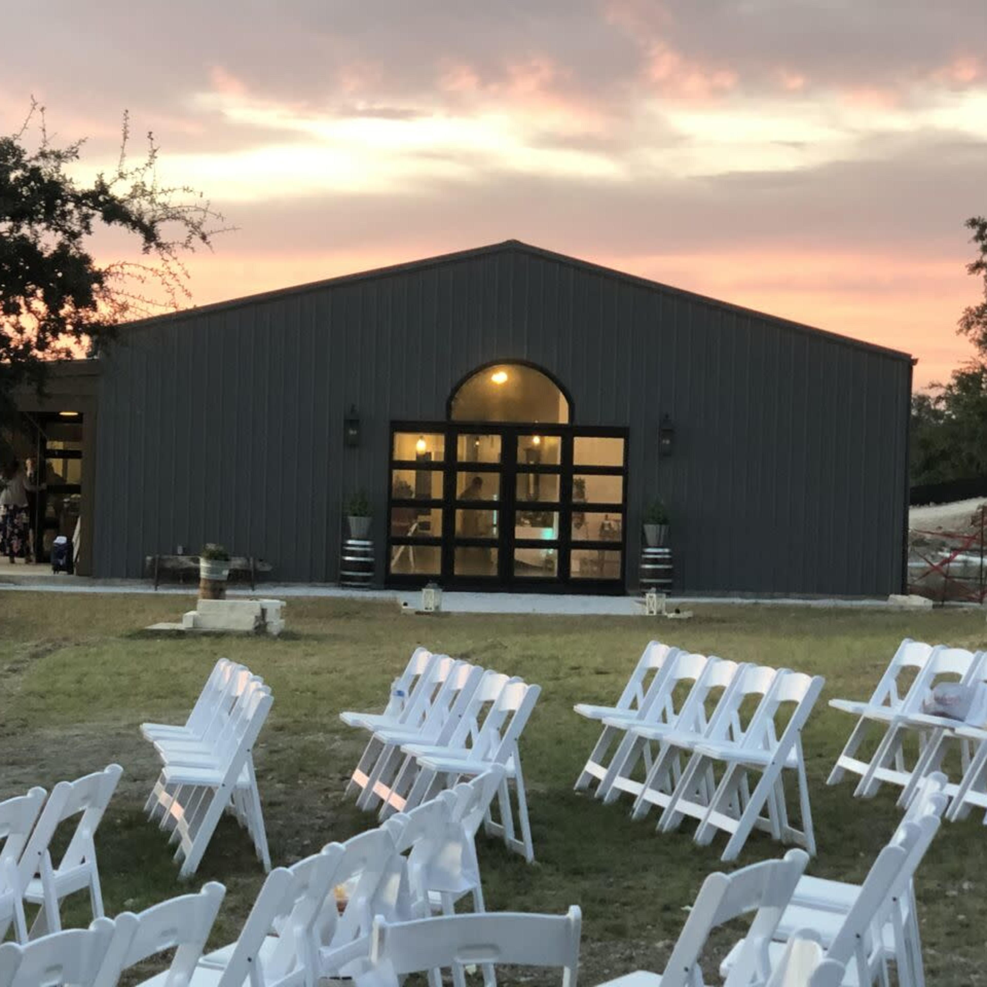 A newly constructed venue sits in the background, with white chairs arranged in rows for an outdoor event as the sun sets.