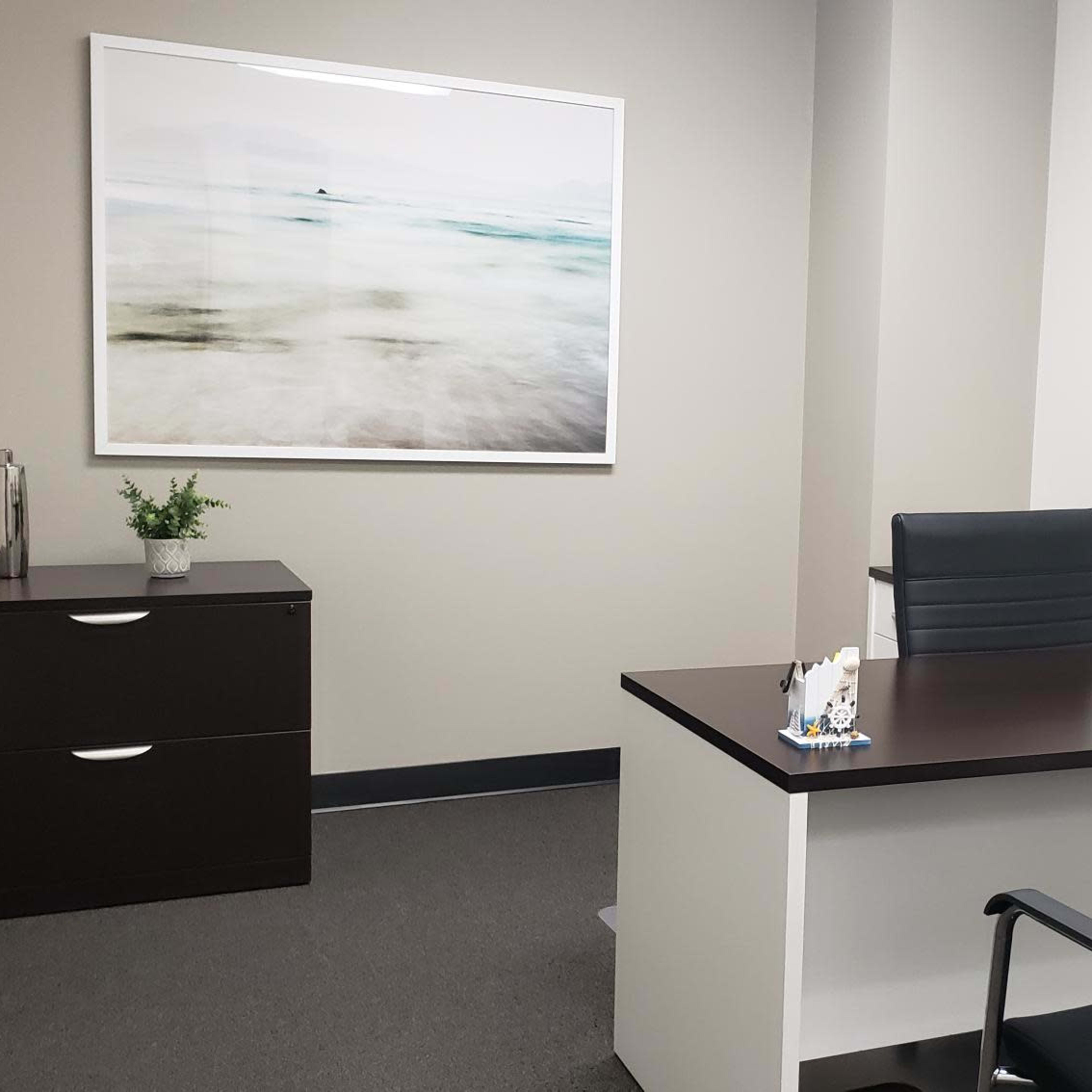 A modern office space features a desk with a chair, a storage cabinet, and a wall-mounted artwork.