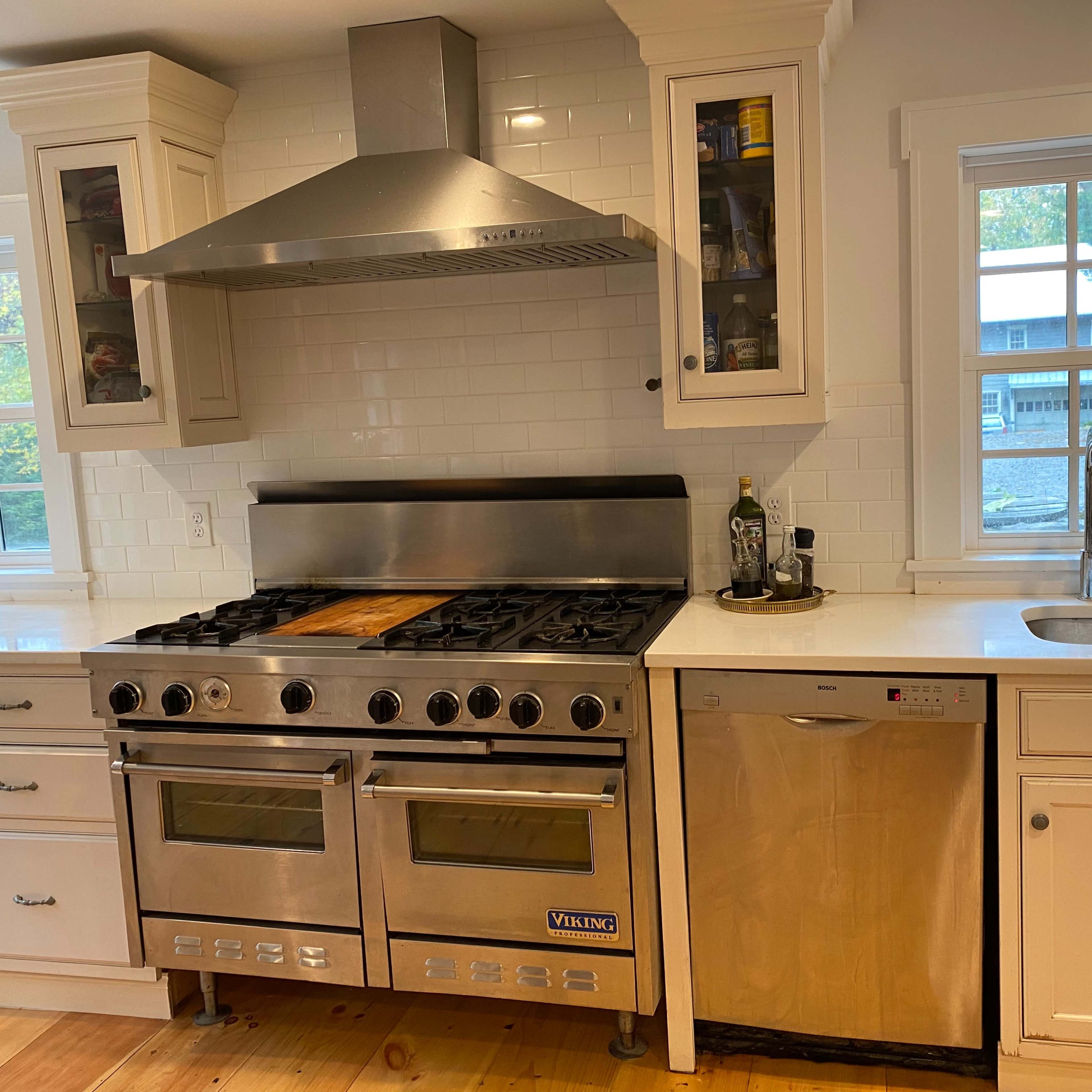 A kitchen featuring a stainless steel Viking range, a dishwasher, and a sink under a window, with white cabinetry and wood flooring.