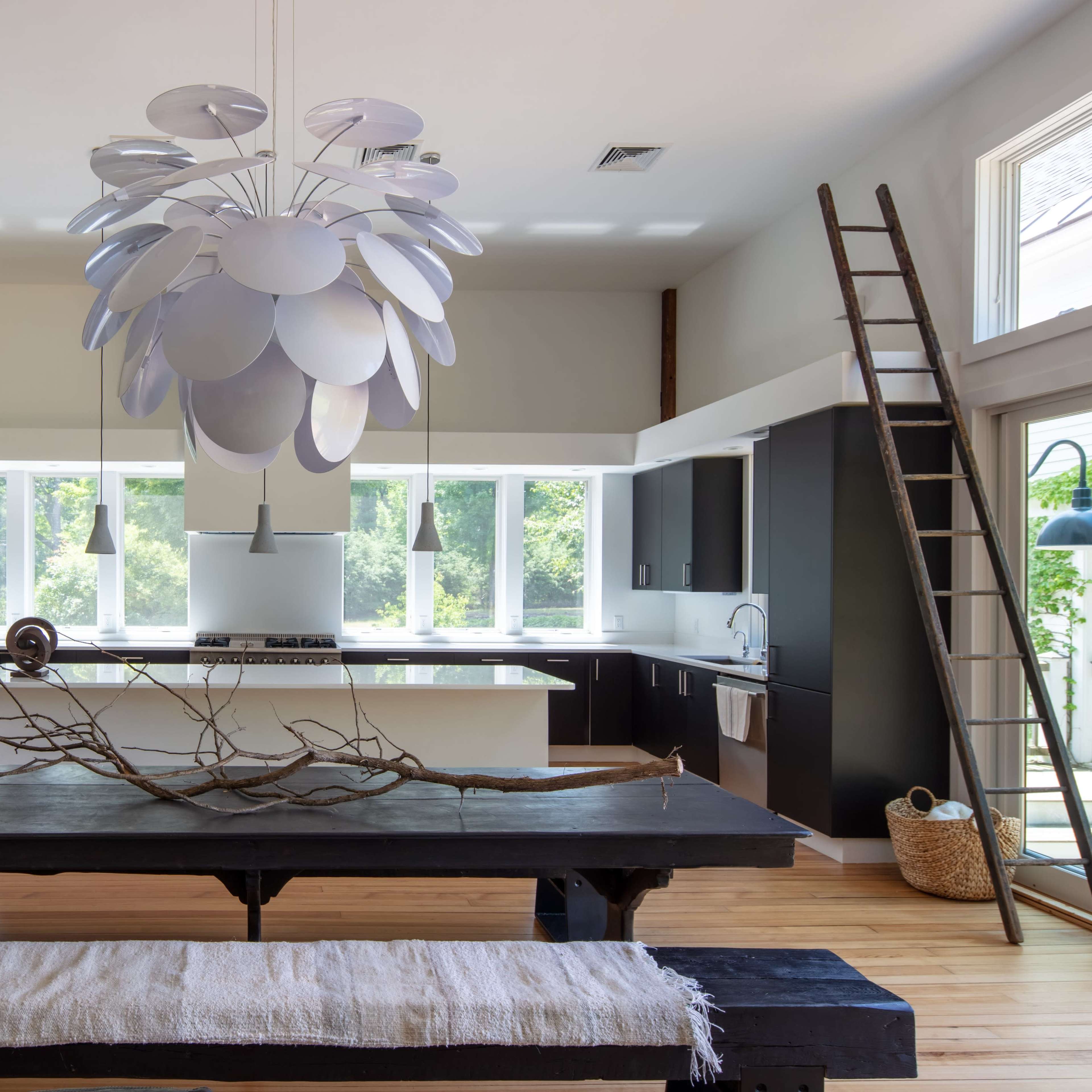 A modern kitchen featuring a large wooden dining table, a unique pendant light, and a ladder against the wall.