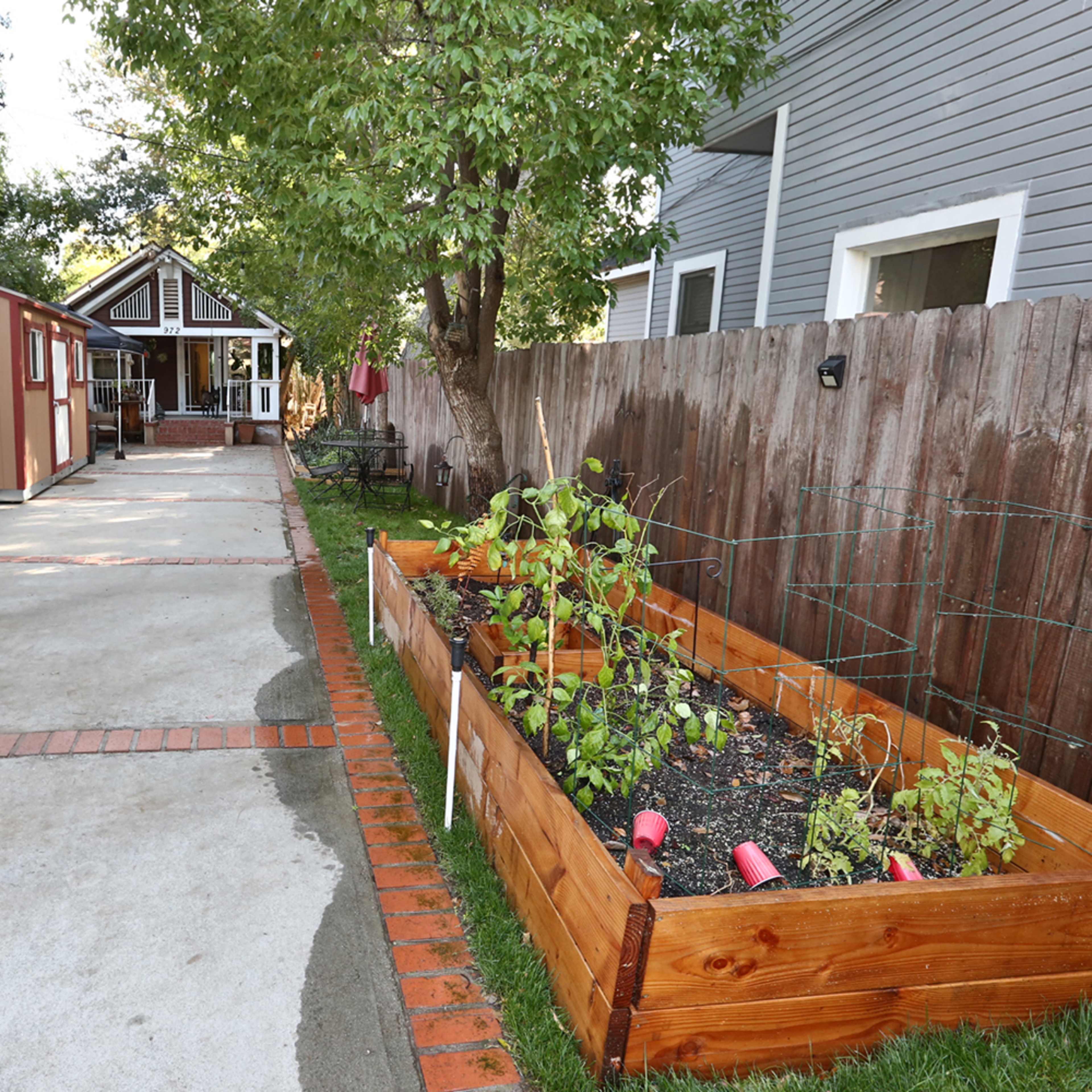 A white van is parked next to a garden bed with plants along a brick-paved driveway beside a house.
