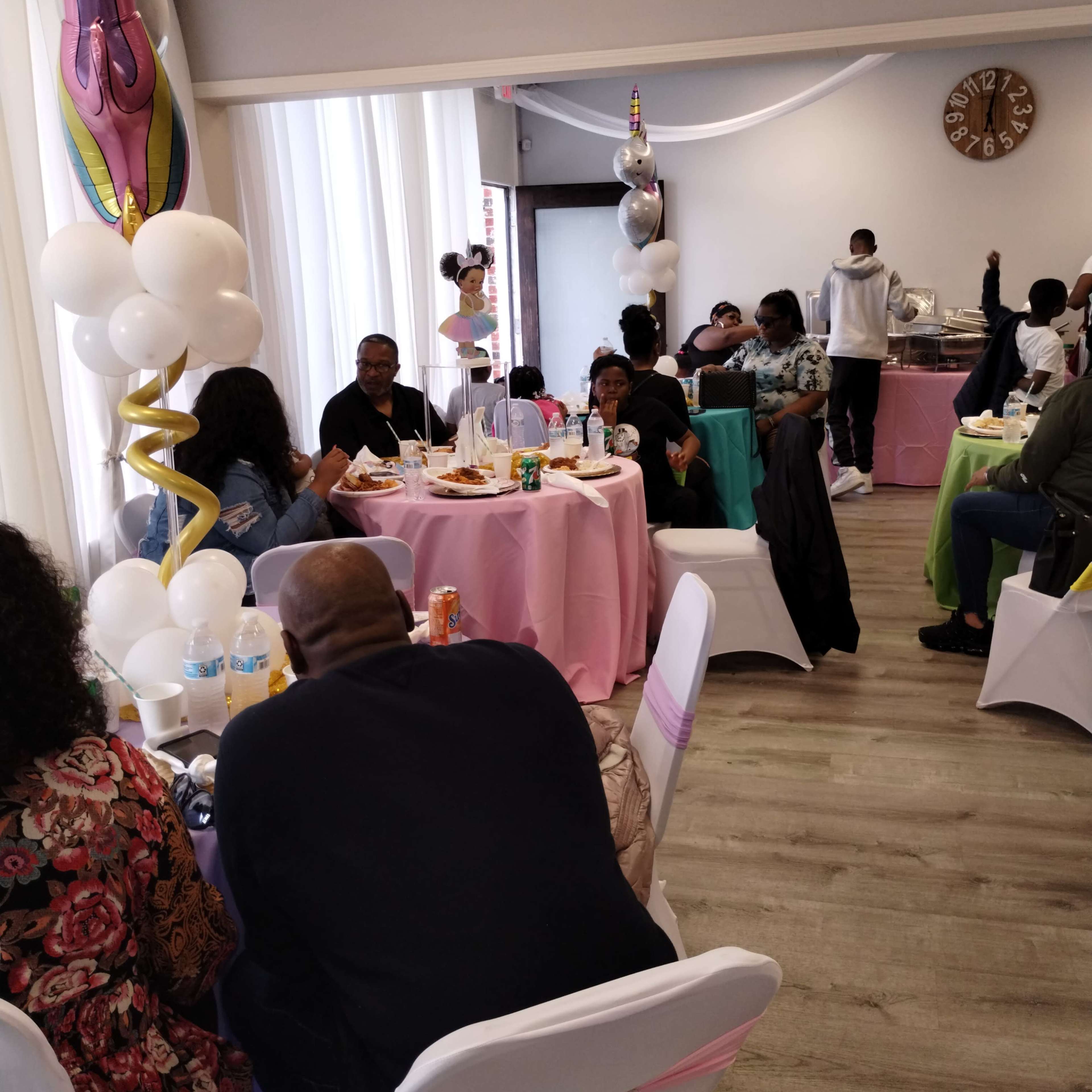 A lively indoor gathering with guests seated at round tables adorned with colorful tablecloths, enjoying food and drinks.