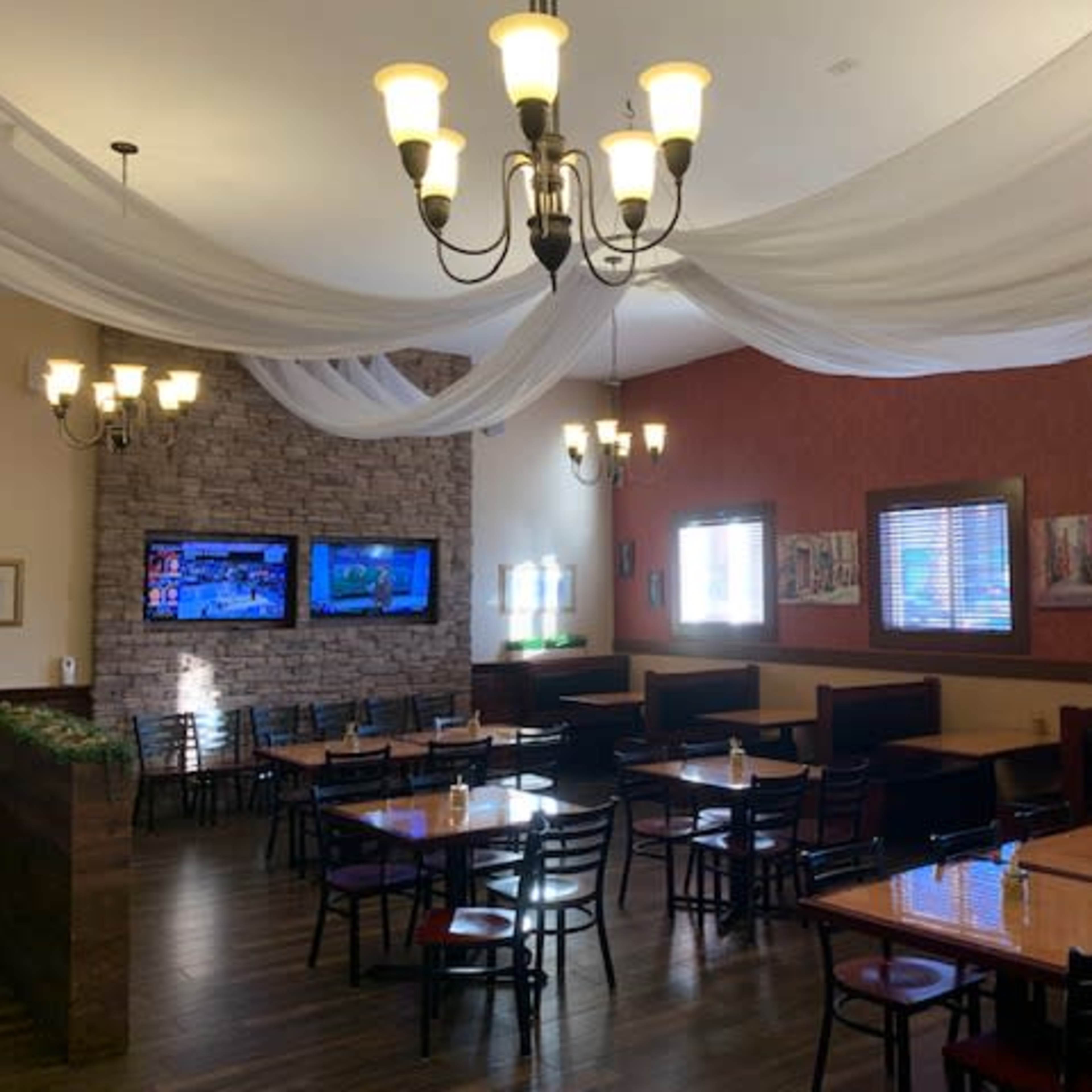 The interior of a restaurant featuring tables, chairs, and decorative lighting with a stone wall and two television screens.