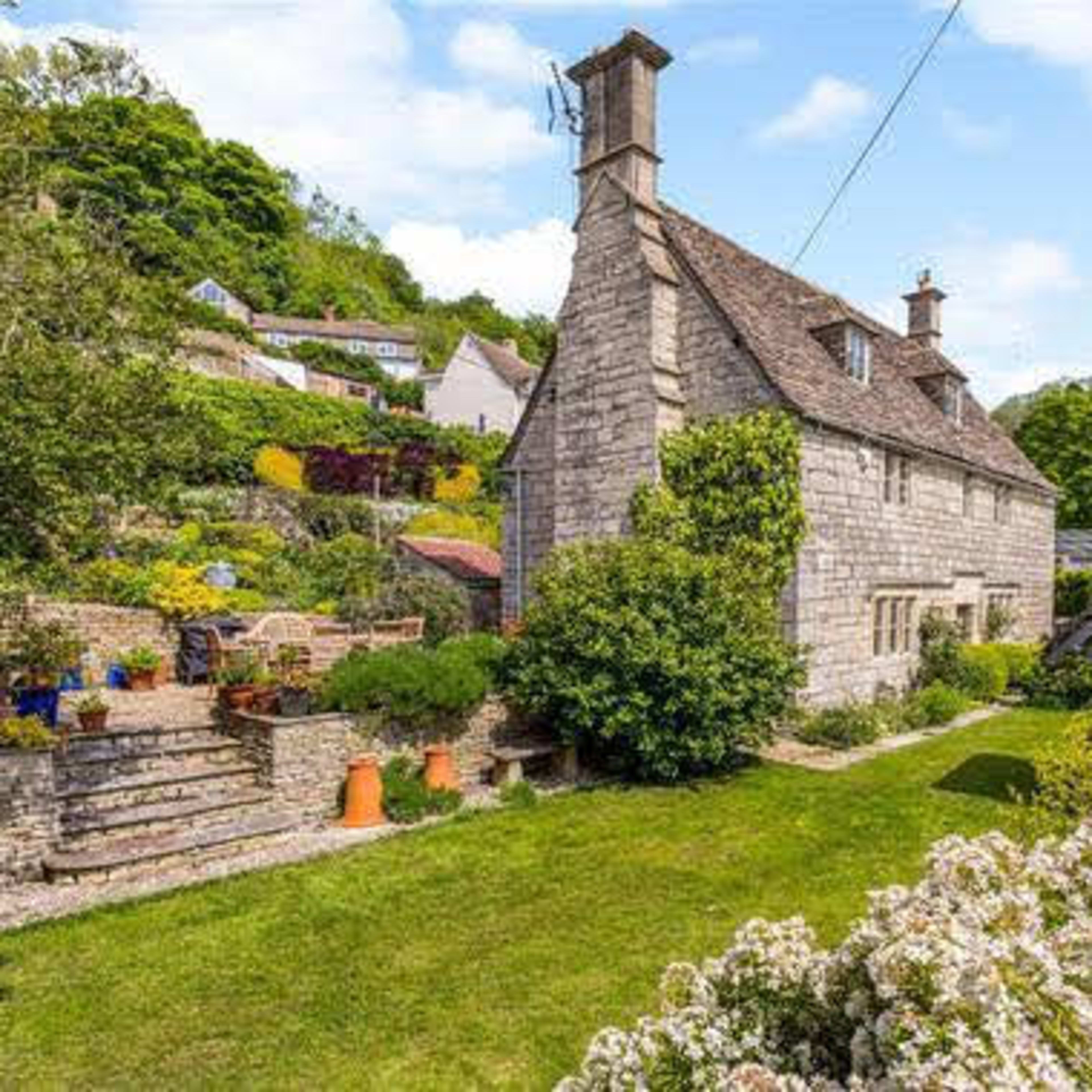 A stone cottage surrounded by a lush garden and landscaped greenery.