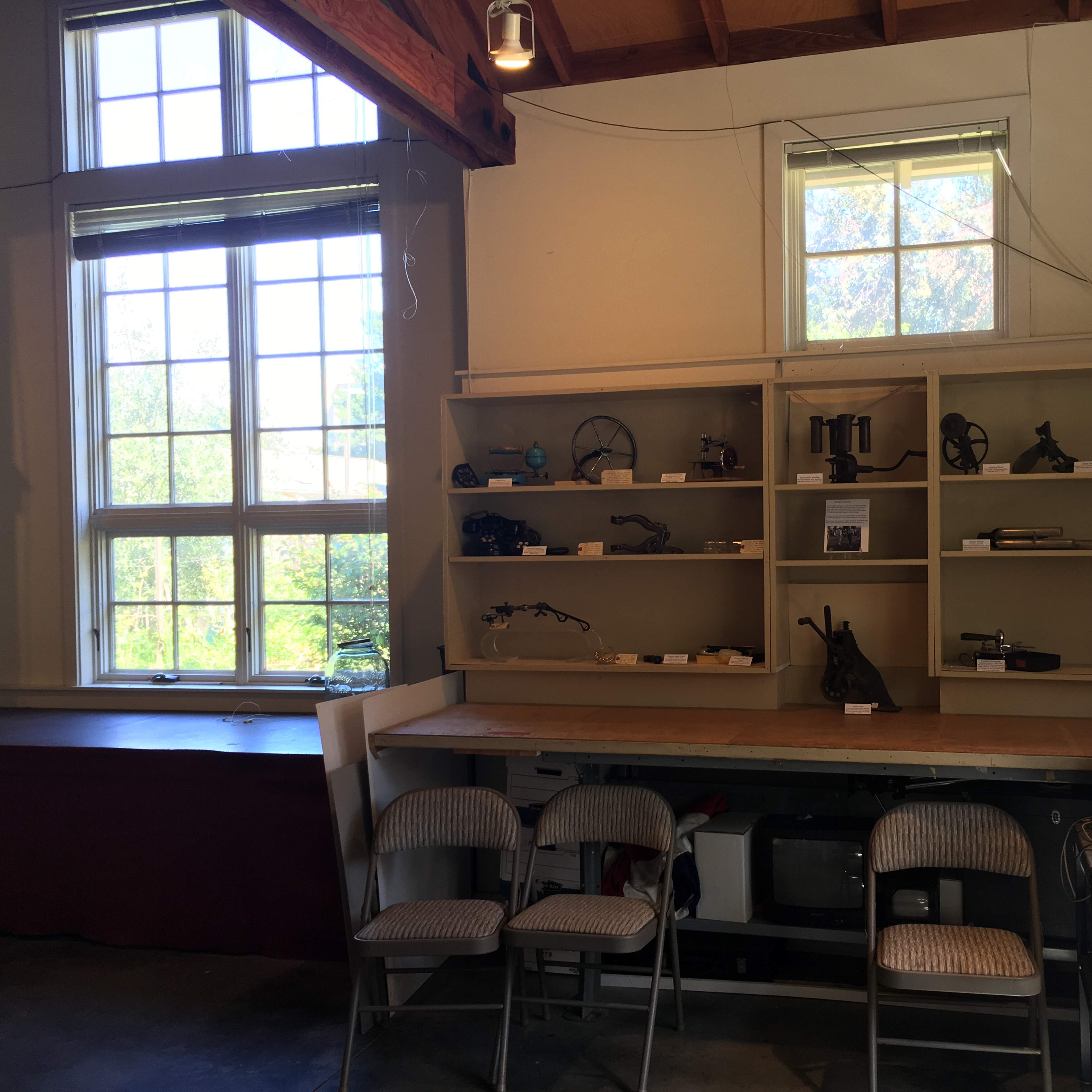 The interior of a room features a shelf displaying various items and tools, along with chairs arranged in front of a counter.