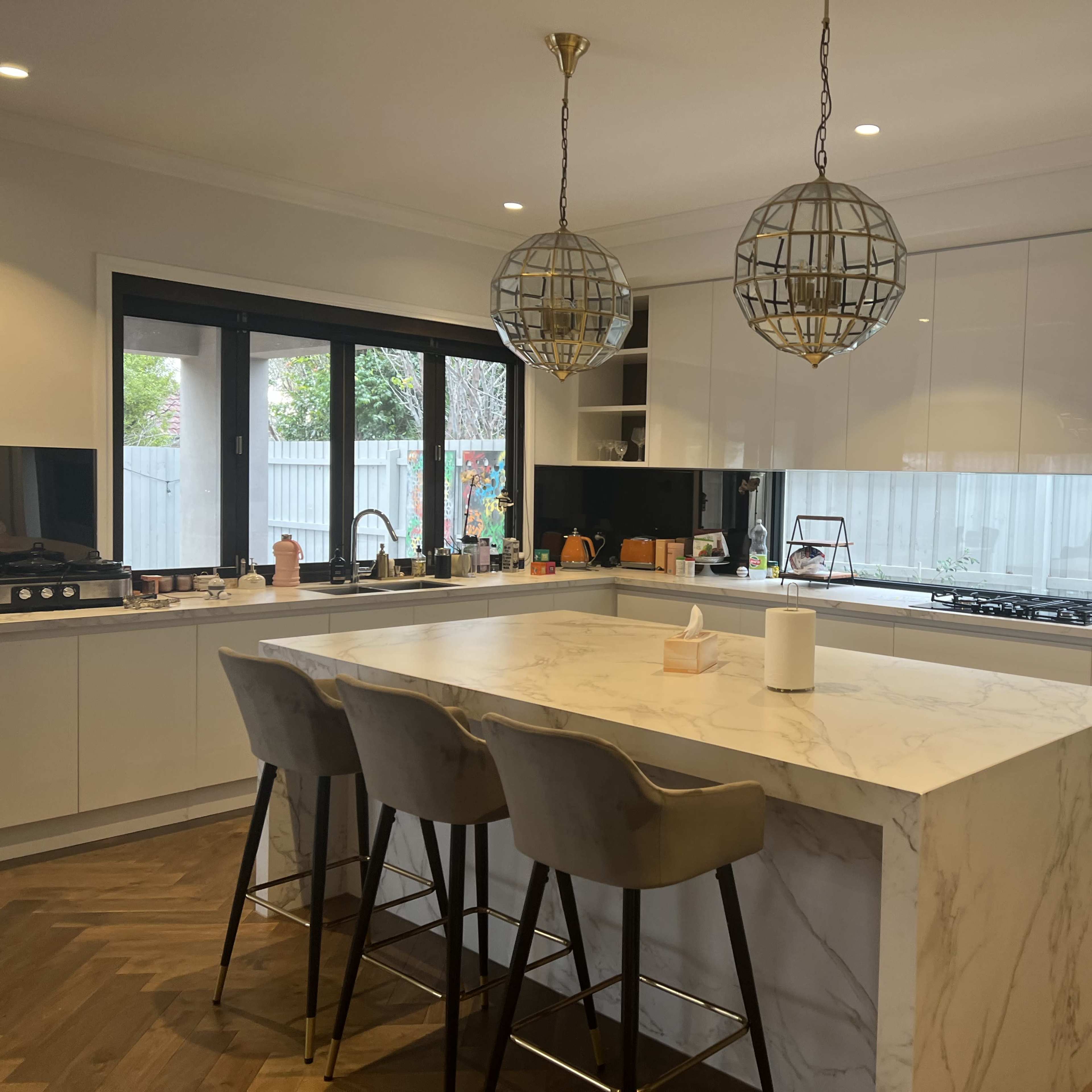 A modern kitchen with a large marble island, three bar stools, and two decorative pendant lights hanging from the ceiling.