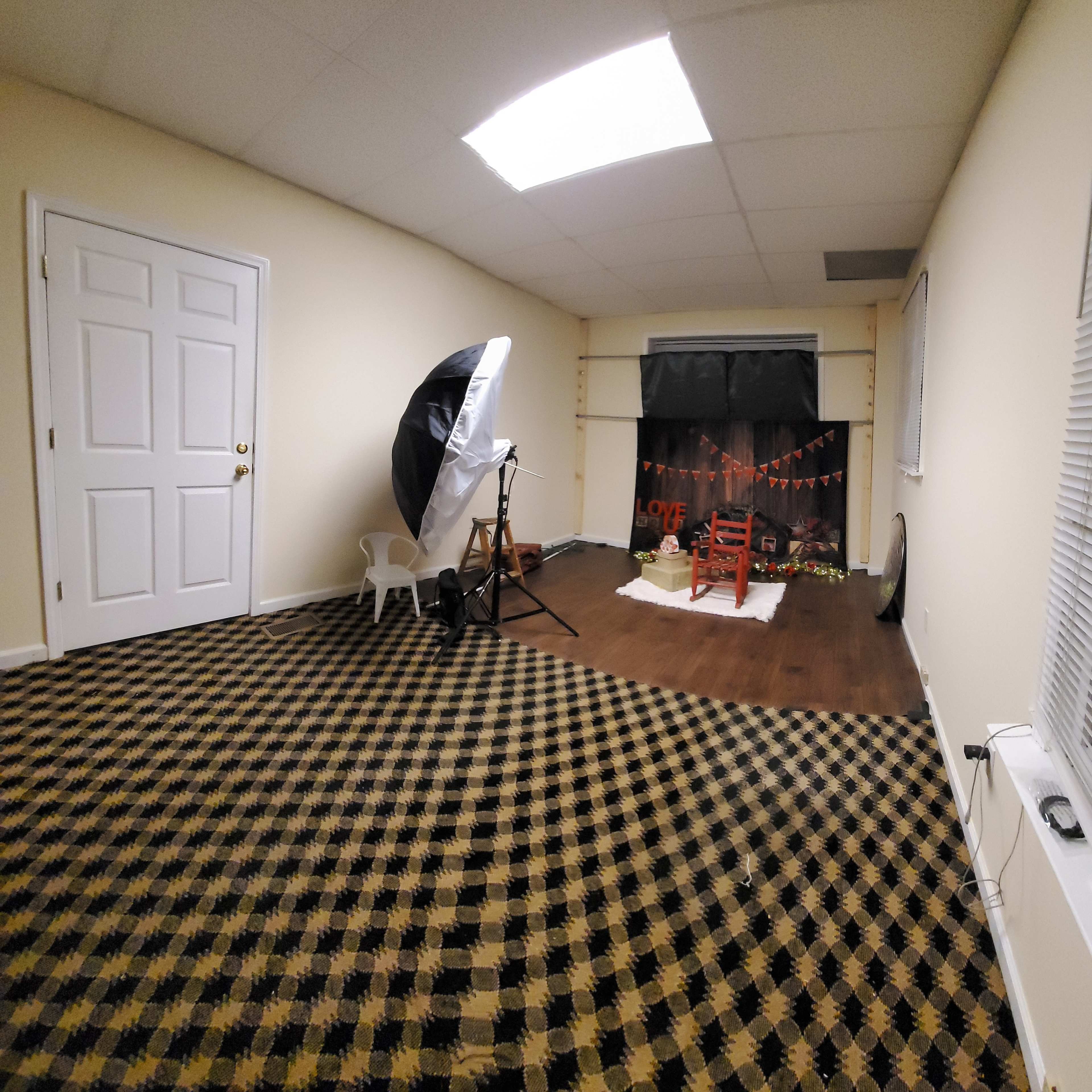 An empty studio space with a checkered floor, a backdrop with decorations, a chair, and photography equipment set up for a shoot.