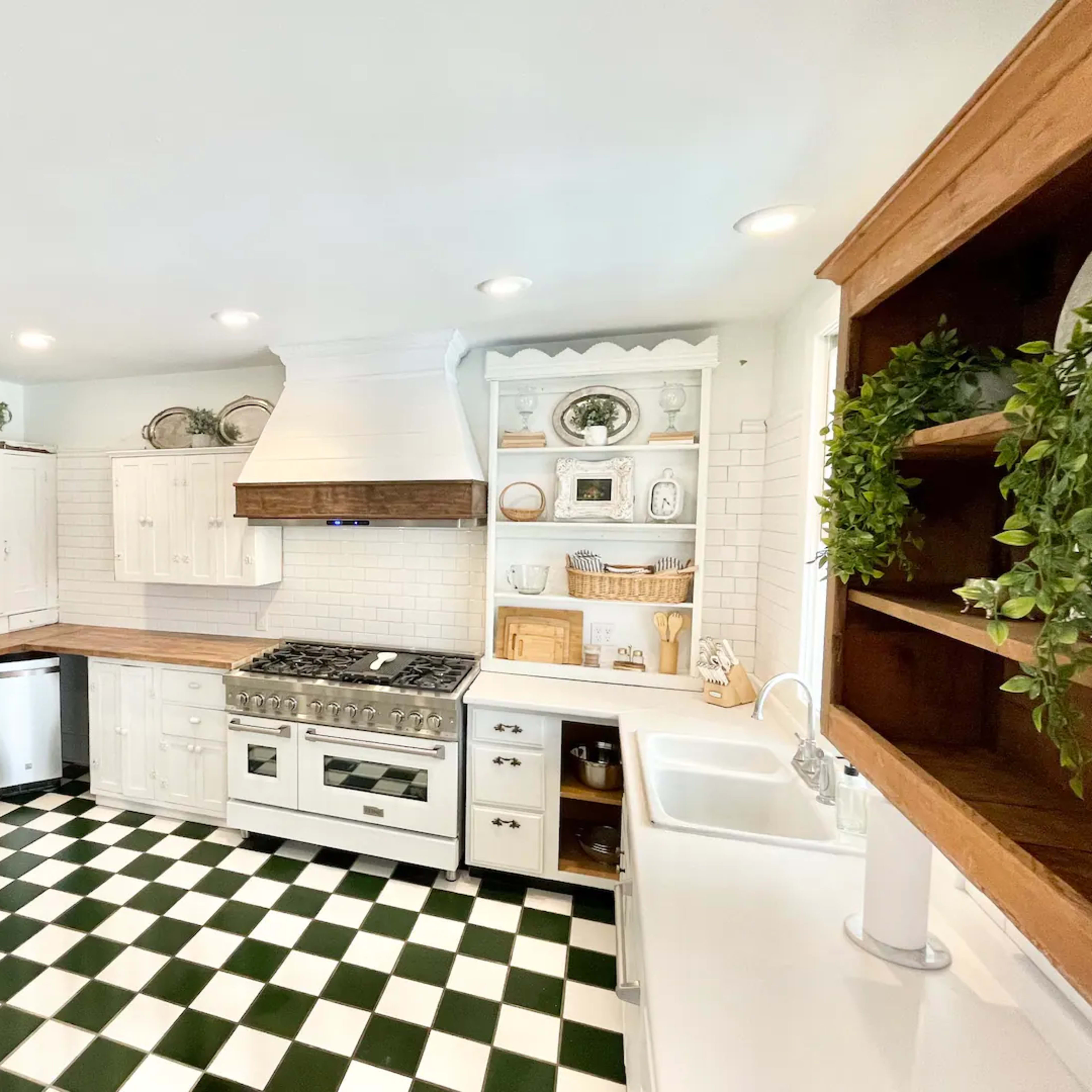 The kitchen features white cabinetry, a large gas stove, a farmhouse sink, and a checkerboard floor with green and white tiles.