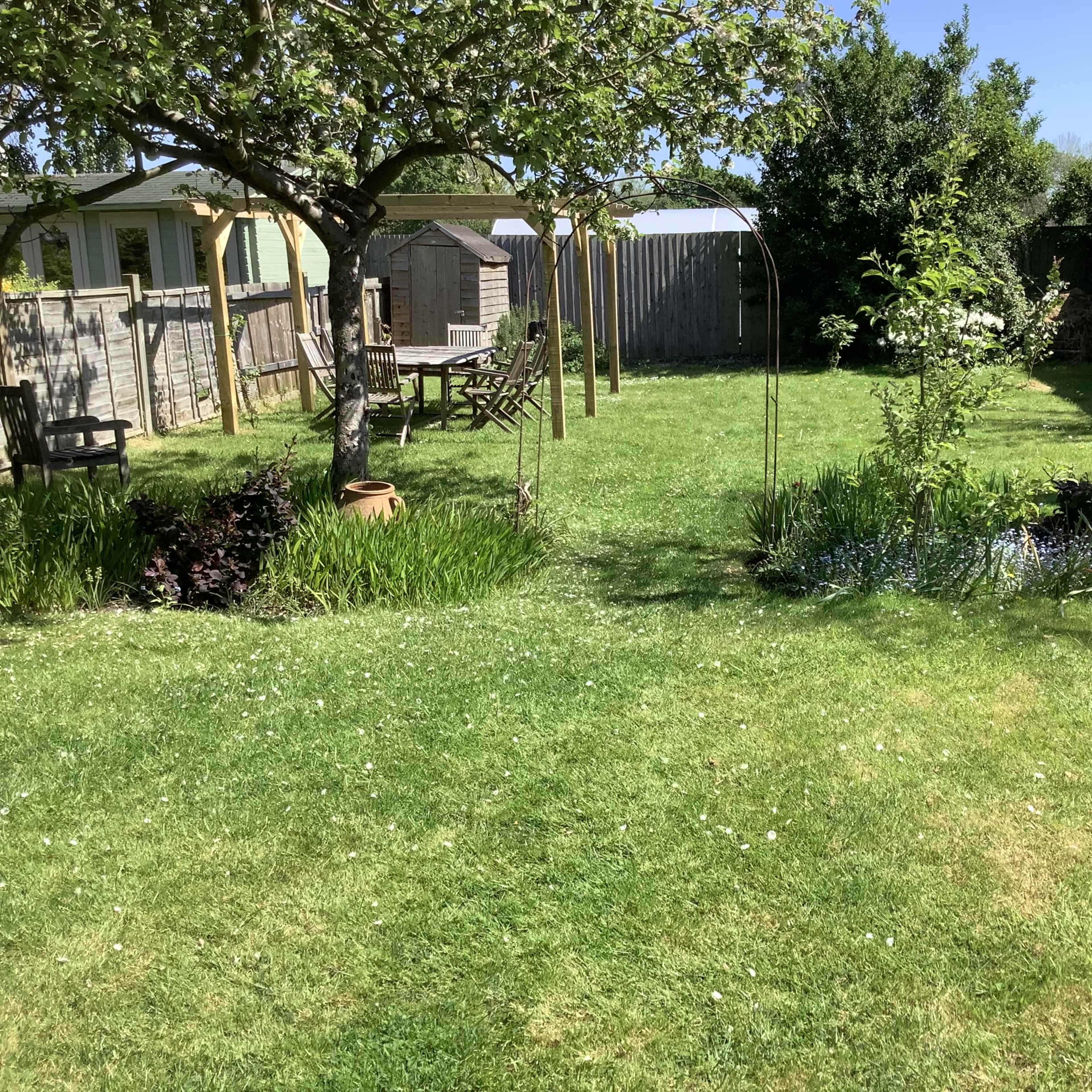 A well-maintained garden features a grassy lawn, a wooden gazebo, a pond with flowering plants, and various trees and shrubs.