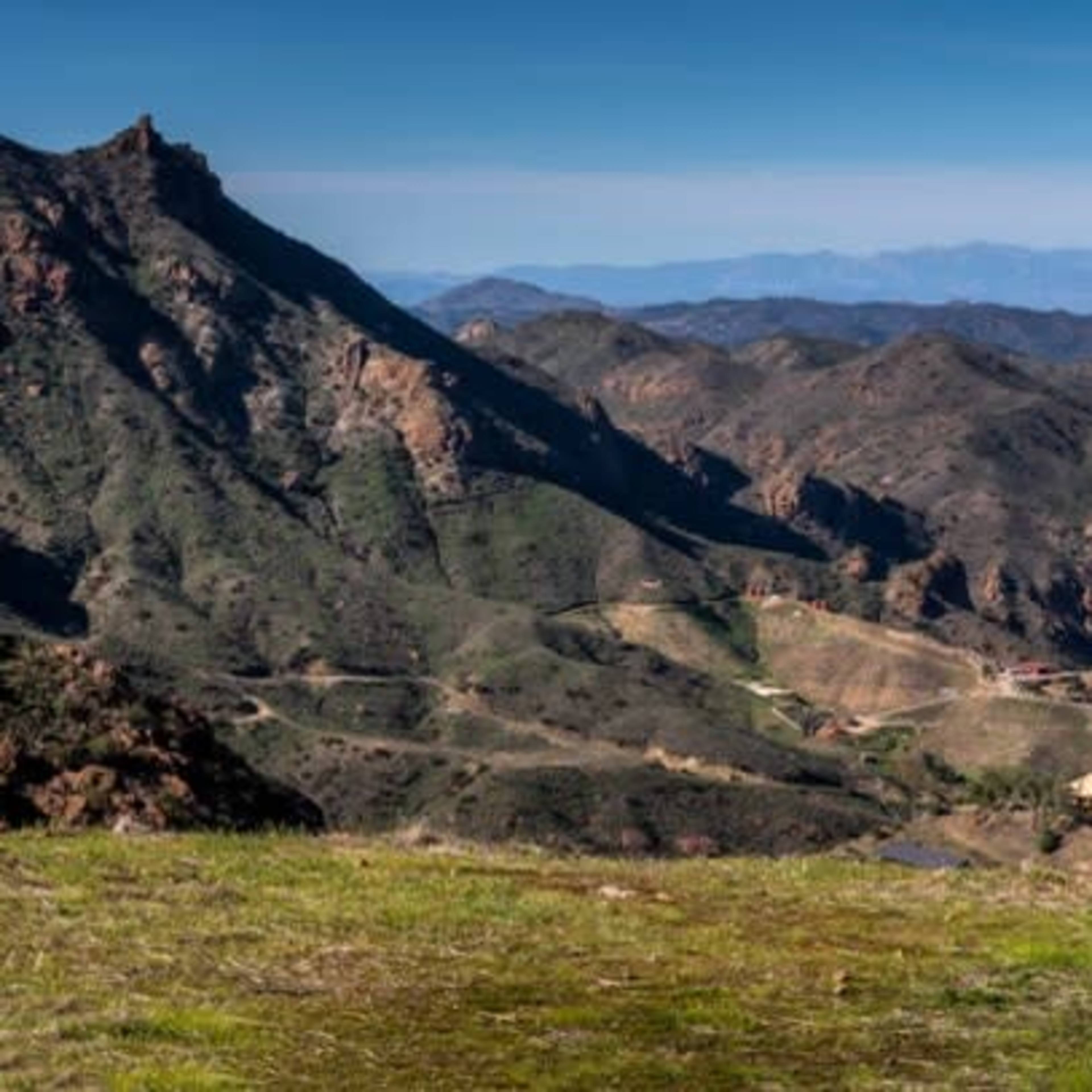 A panoramic view of rolling hills and rocky terrain under a clear blue sky.