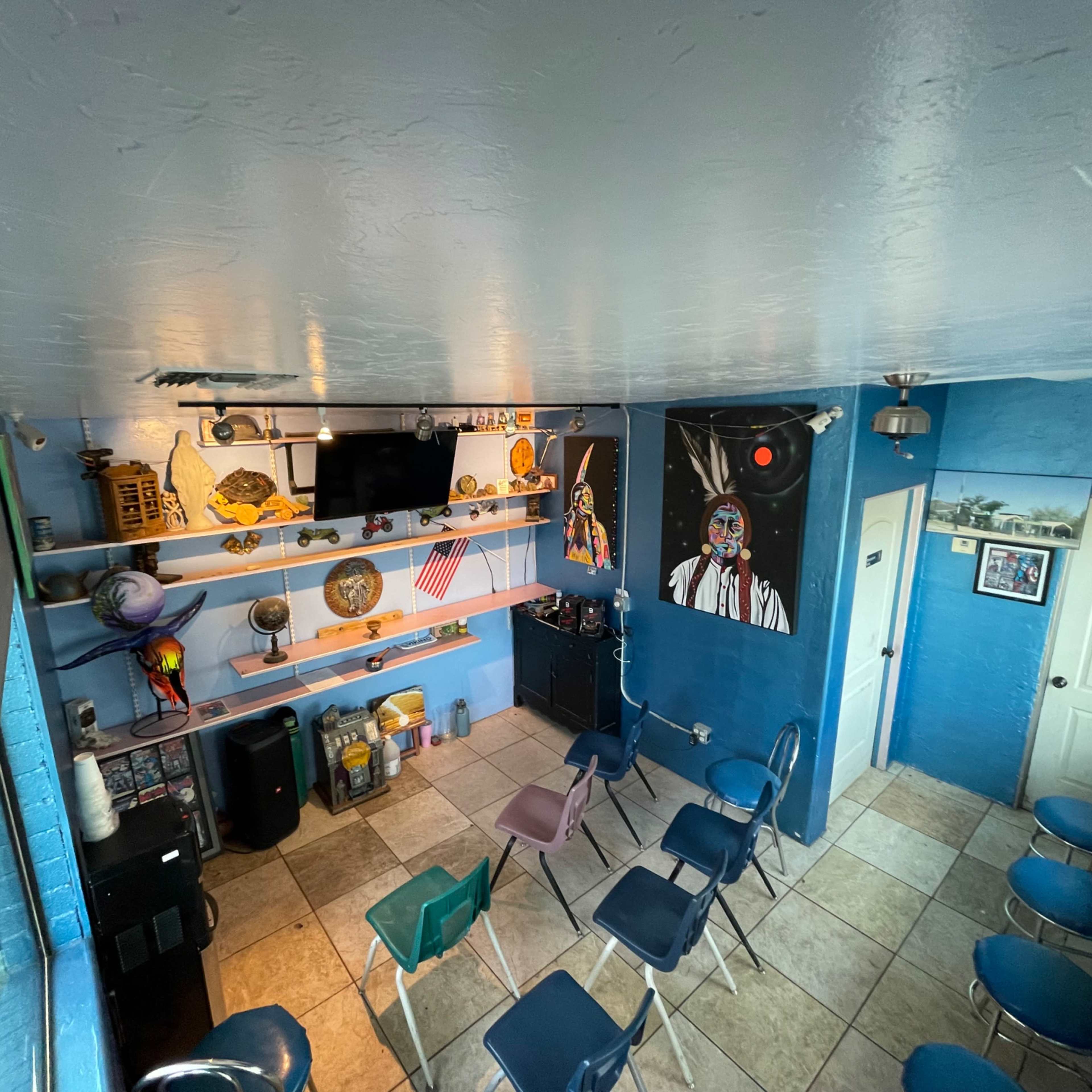 A small room with blue walls, arranged with several chairs facing a wall displaying a television and various decorations, including an American flag and artwork.