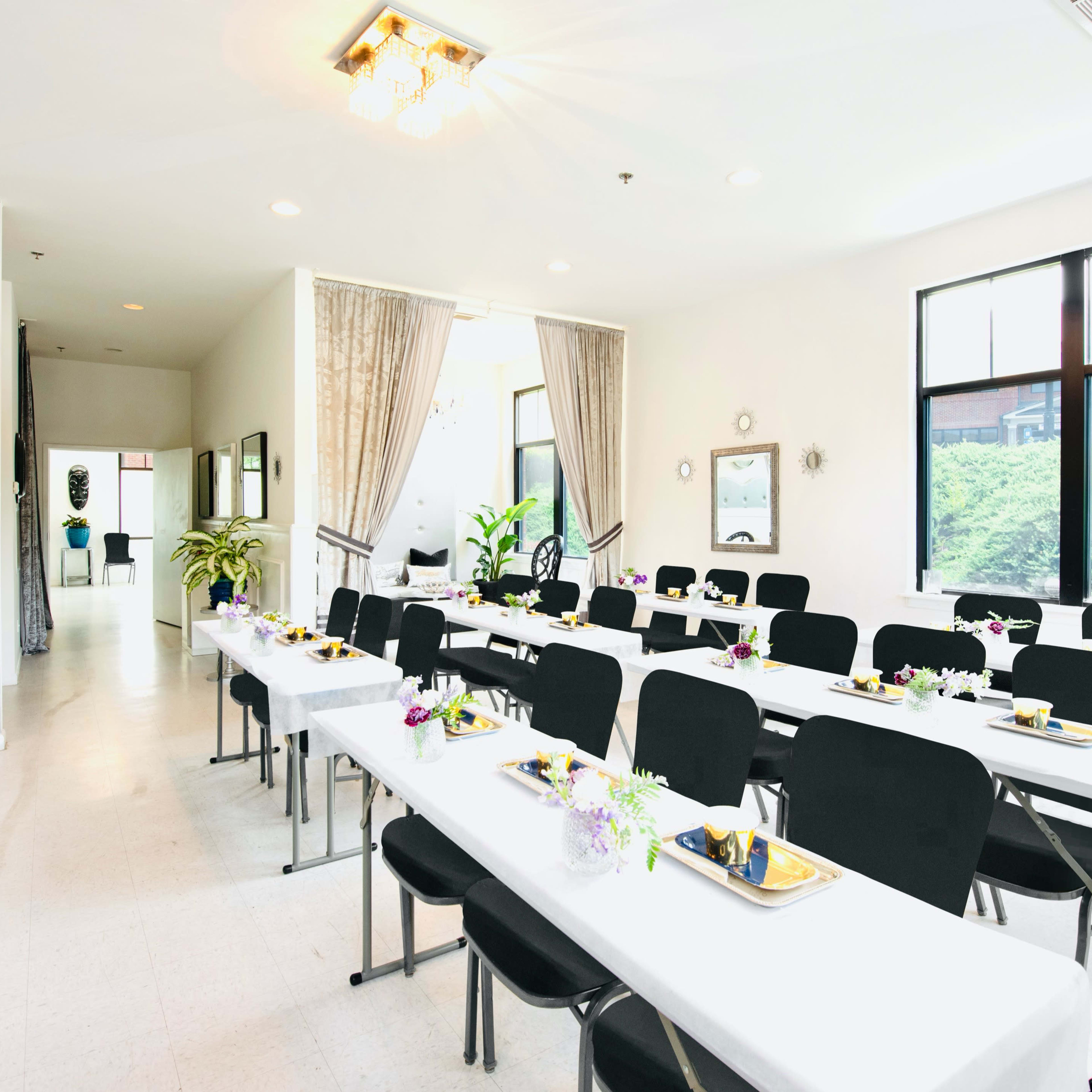 A well-organized indoor banquet room features several rows of tables set for a meal with black chairs and floral centerpieces.