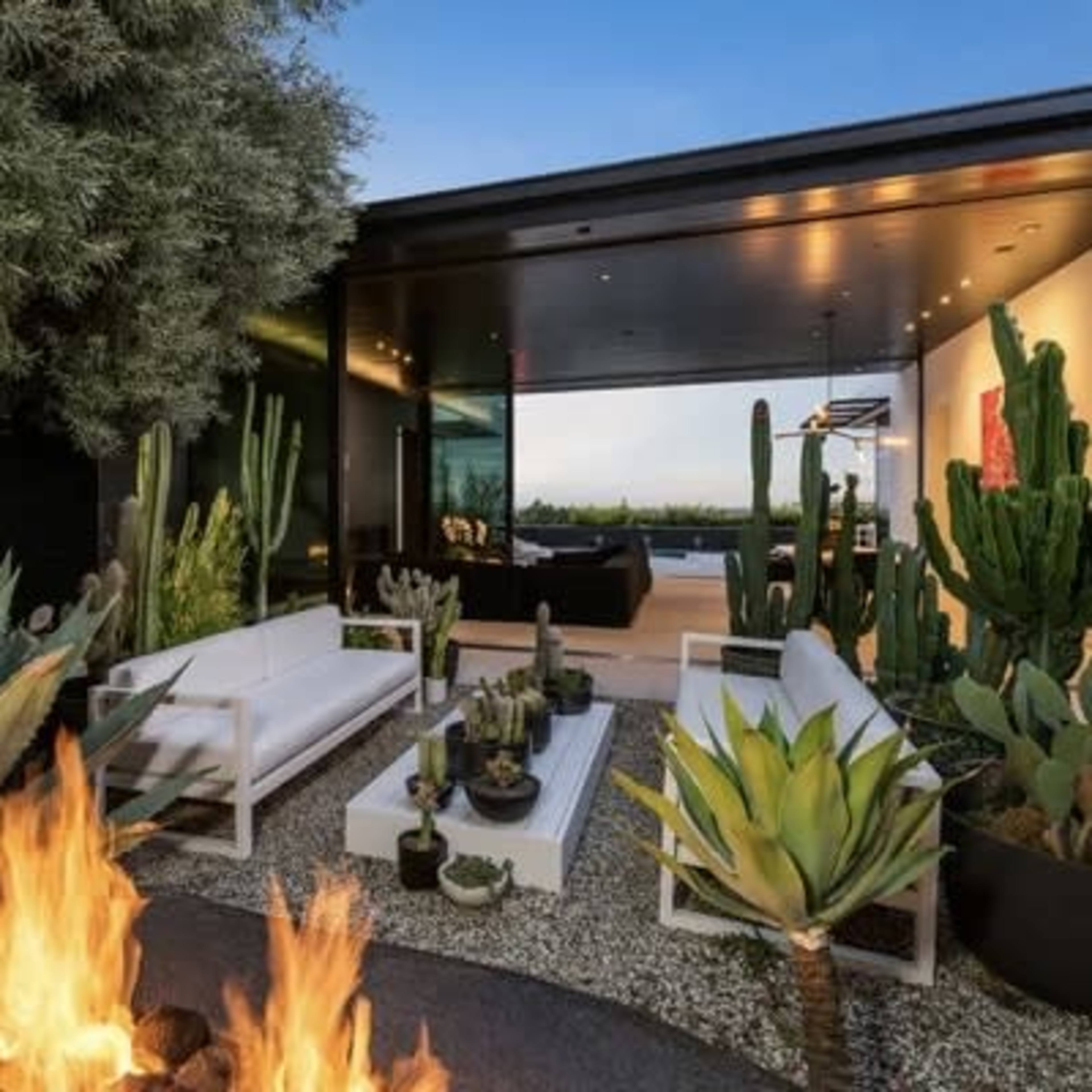 A modern outdoor living space features white seating surrounding a fire pit, surrounded by various cacti and plants.