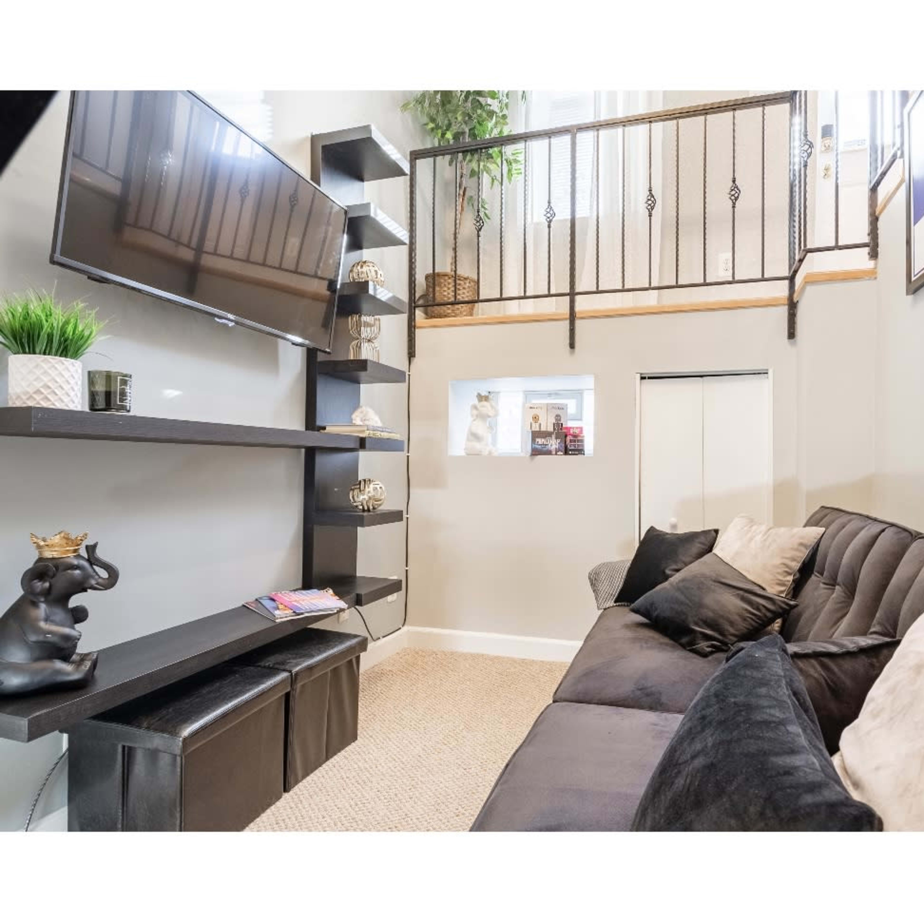 A modern living room with a black sofa, a wall-mounted television, and a shelving unit against the wall.