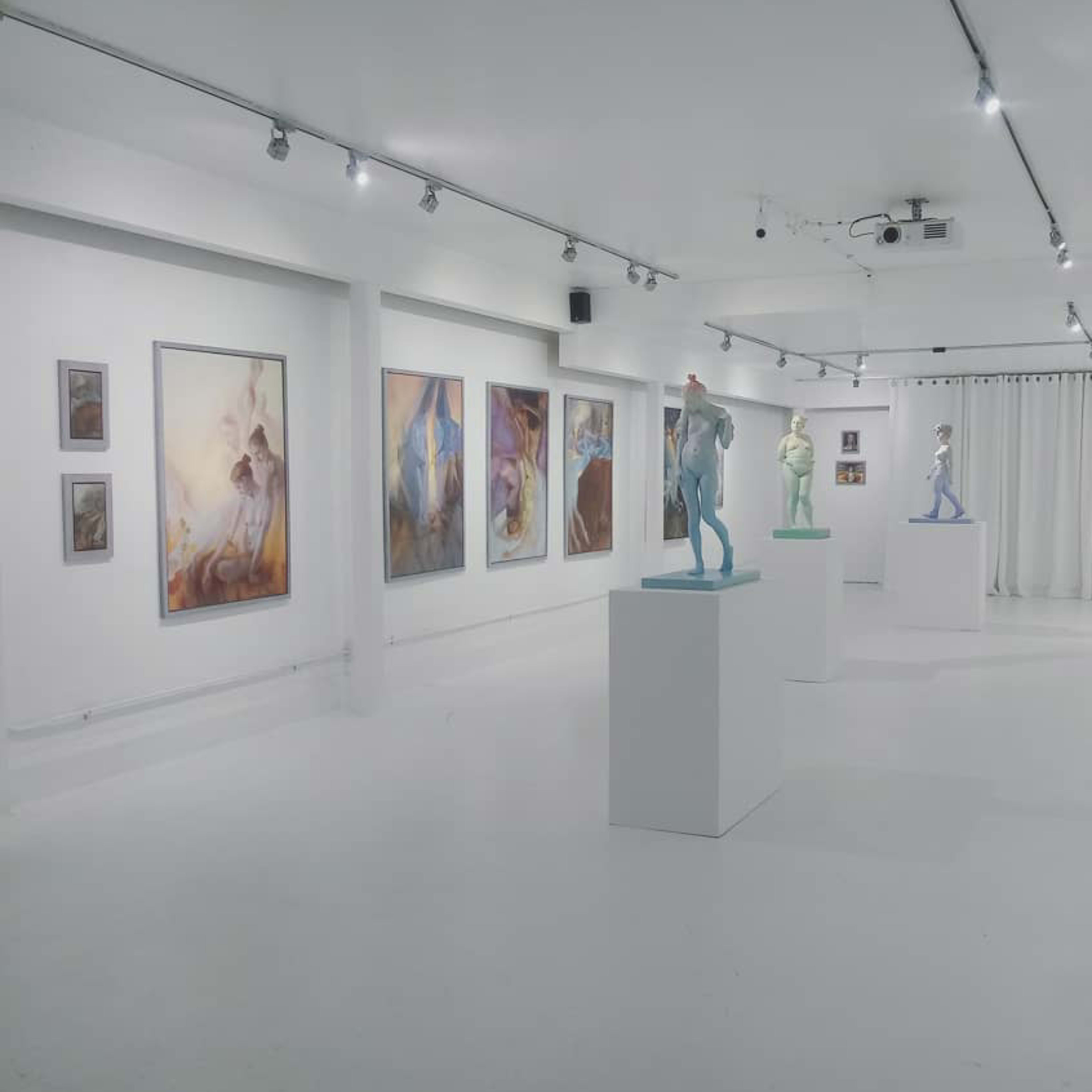 A modern art gallery featuring several sculptures on pedestals and various paintings displayed on the white walls.
