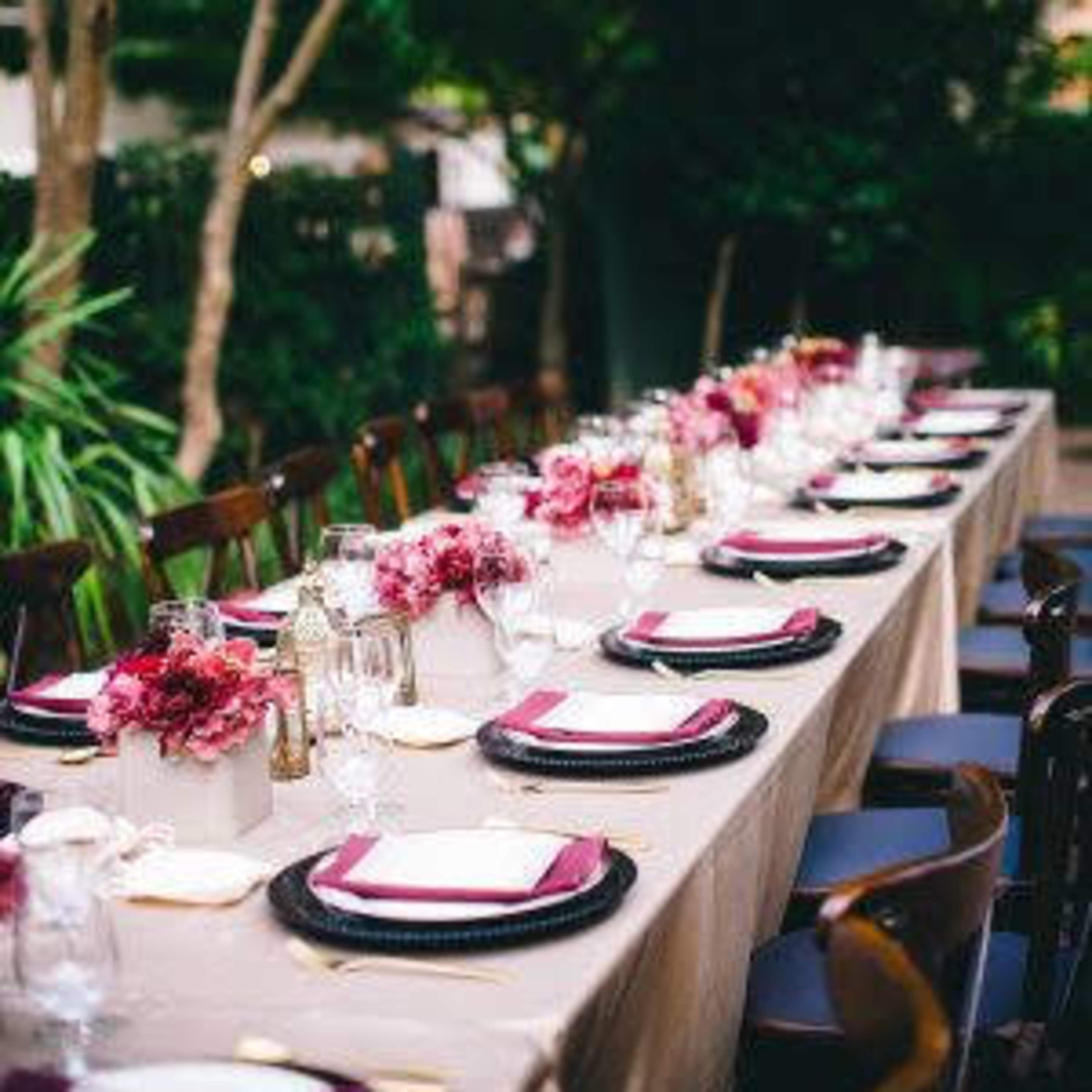 A long dining table set outdoors is adorned with floral centerpieces and neatly arranged plates and glassware.