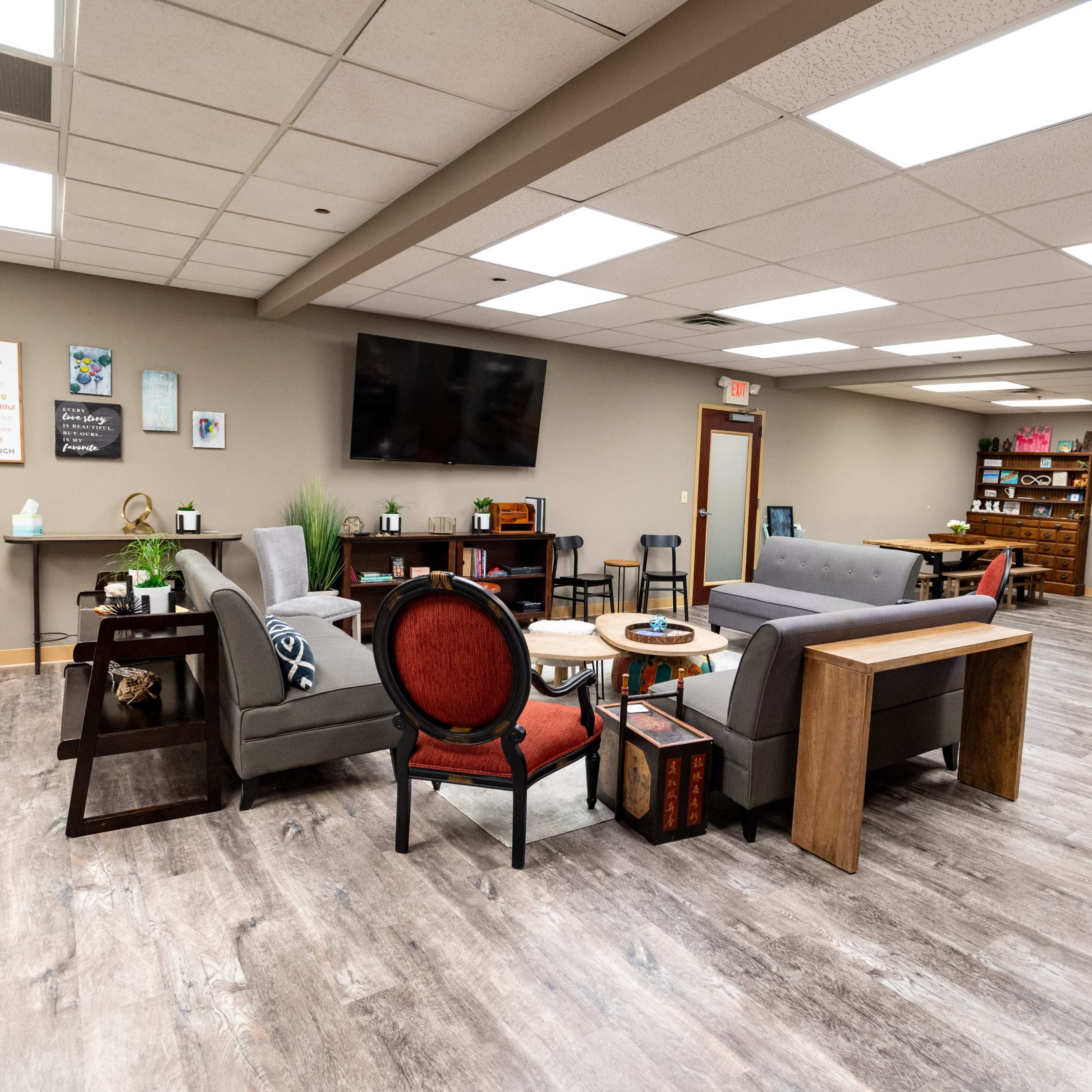 A modern lounge area with two sofas, a red chair, a coffee table, and a large TV mounted on the wall, set in a spacious room with wooden flooring.