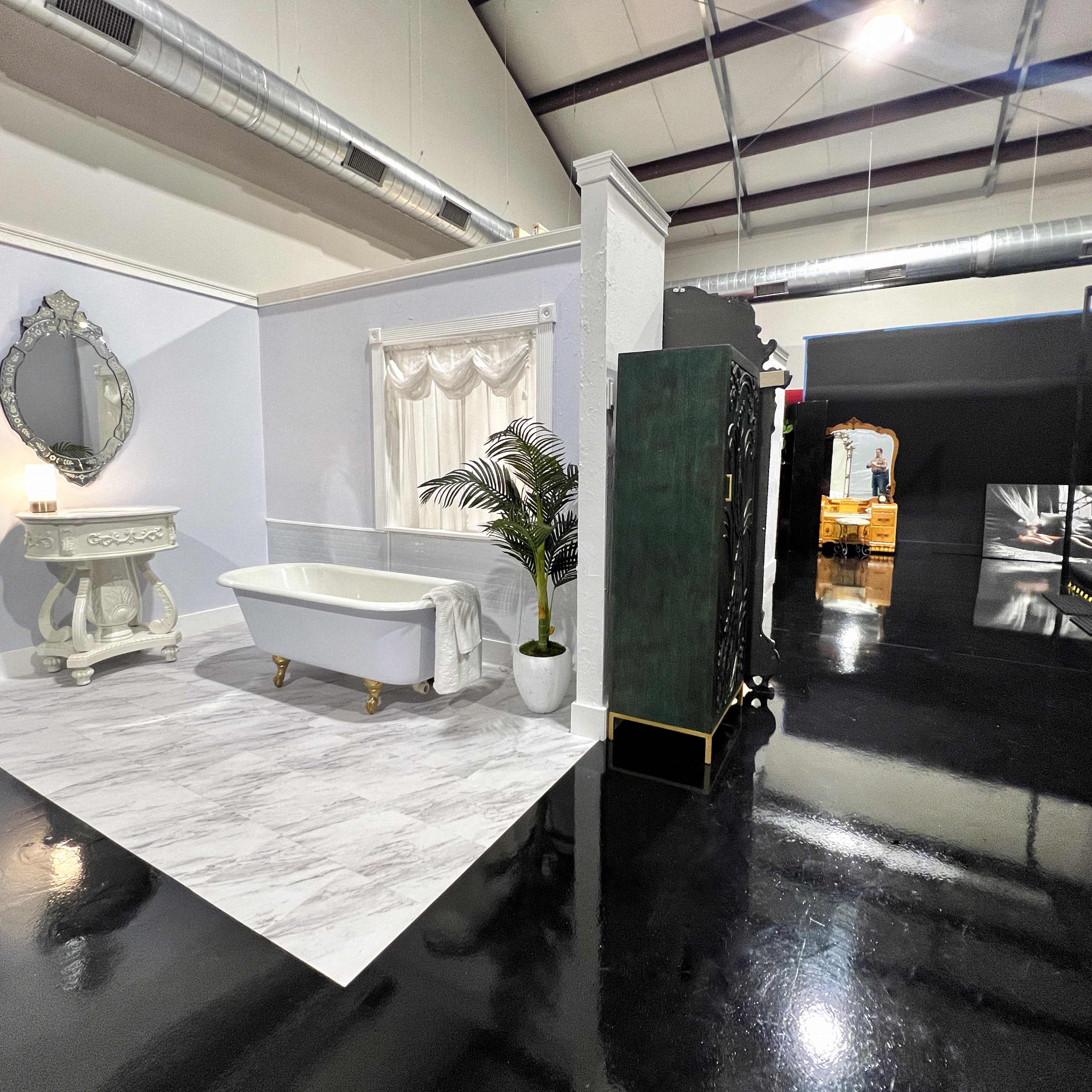 A spacious interior with a white bathtub on a marble-patterned floor, accompanied by a vintage-style mirror and a plant in a corner.