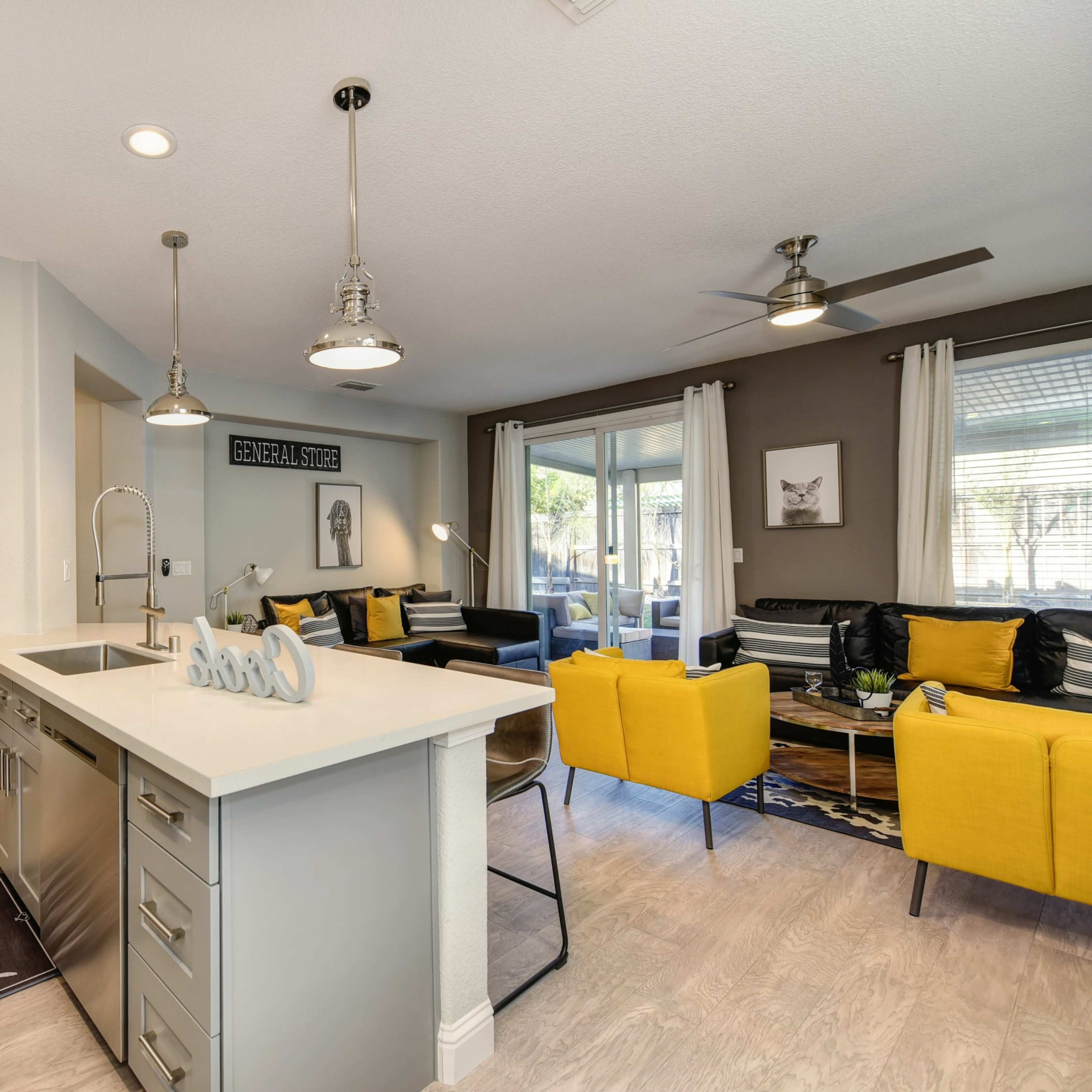 A modern open-concept living space featuring a kitchen with a central island, yellow accent chairs, and a cozy seating area with natural light.
