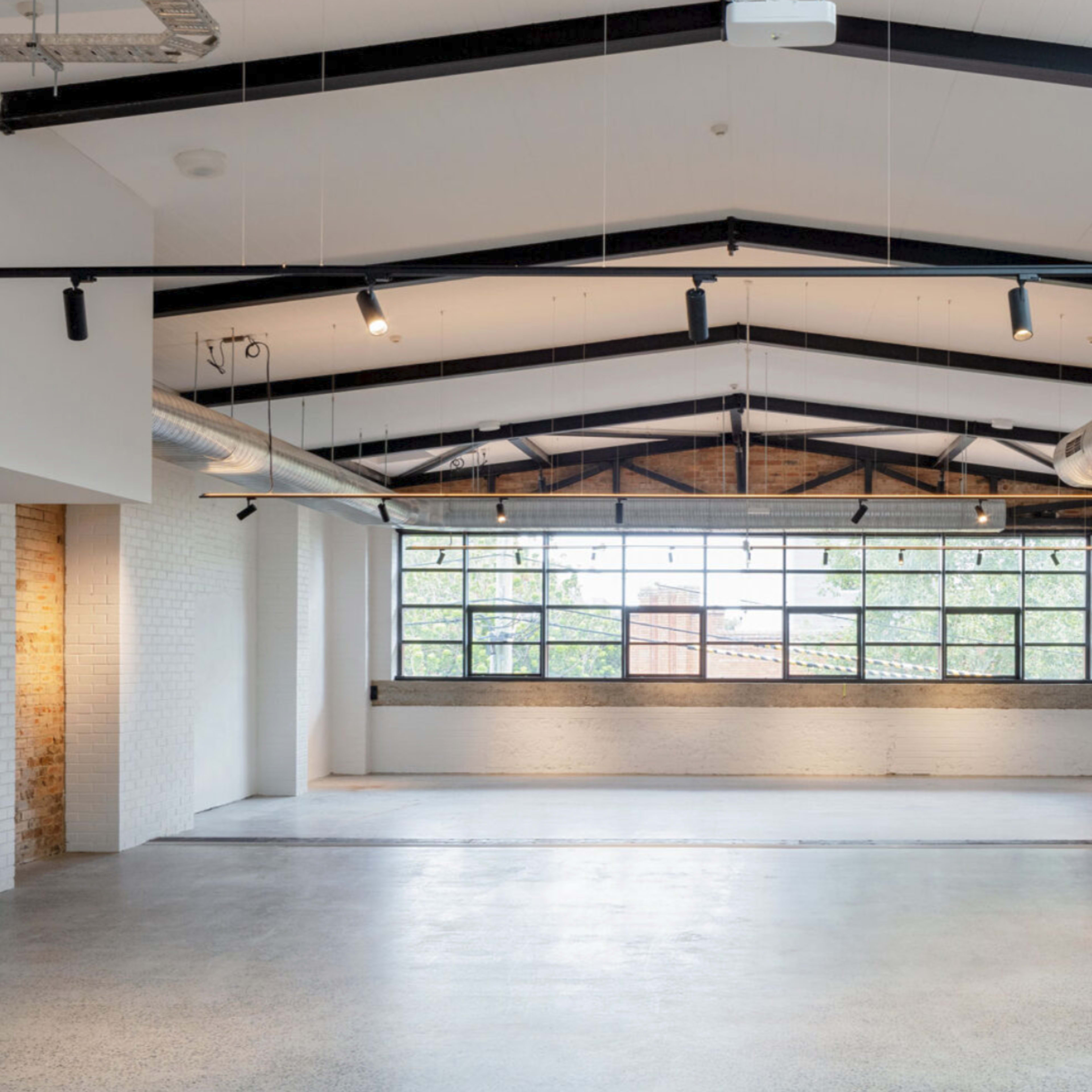 A spacious, industrial-style interior with high ceilings, large windows, and exposed brick walls.