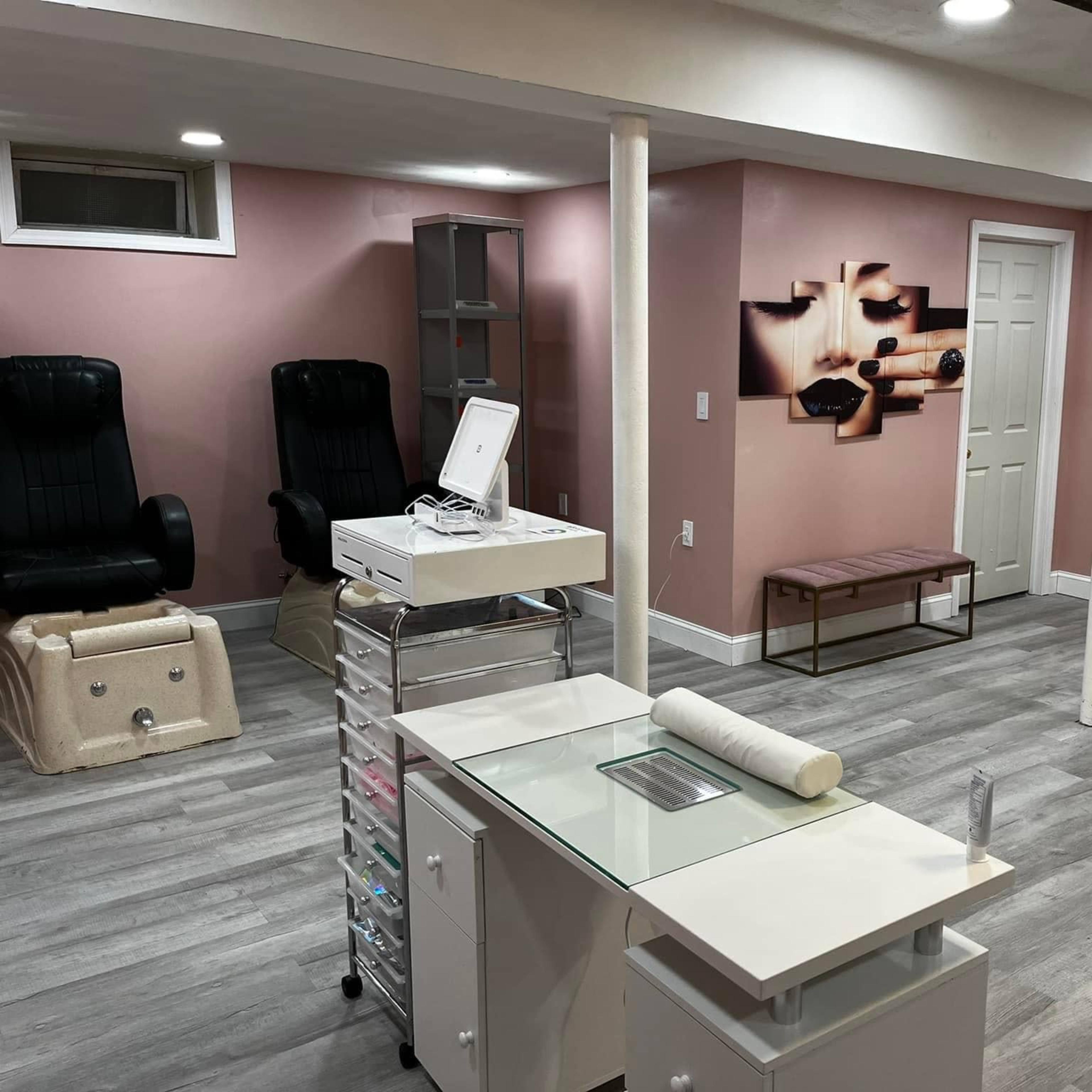 A finished basement with light pink walls, gray flooring, a reception area with a glass-top desk, and seating areas including two dark chairs and a bench.