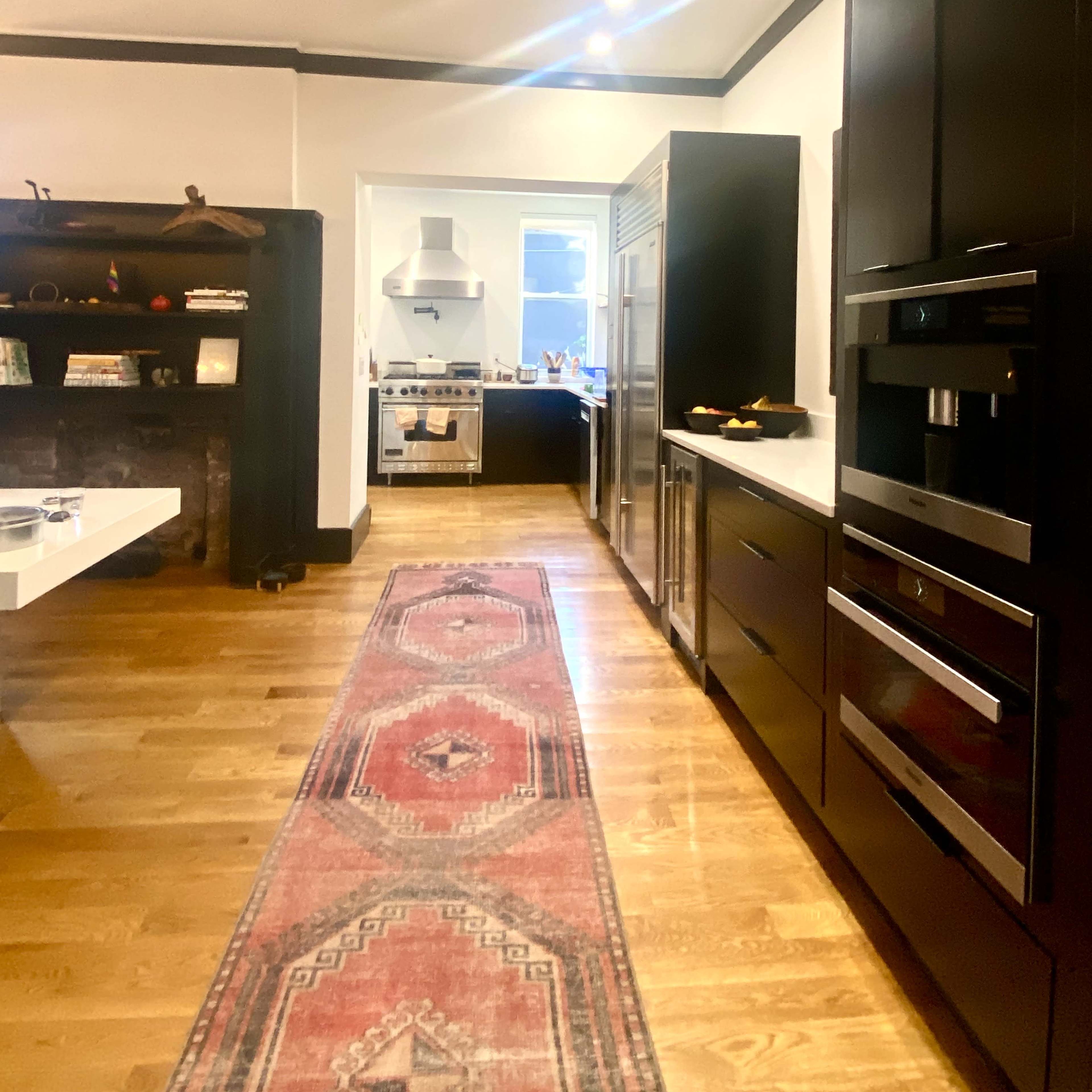 A modern kitchen features dark cabinetry, stainless steel appliances, and a central island, with a patterned runner rug extending down the wooden floor.