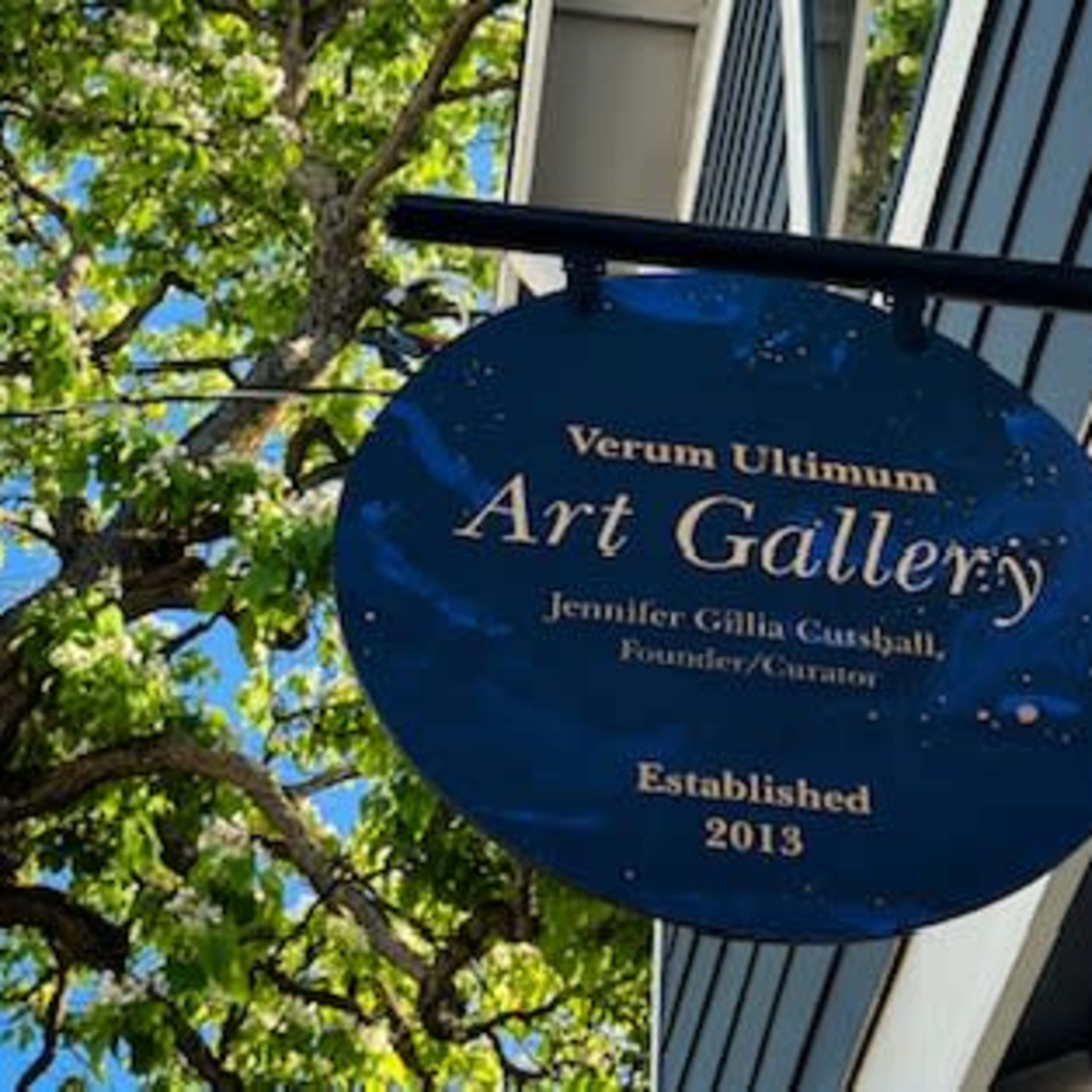 A sign for the "Verum Ultimum Art Gallery," indicating it was established in 2013 and is curated by Jennifer Gila Caspall.