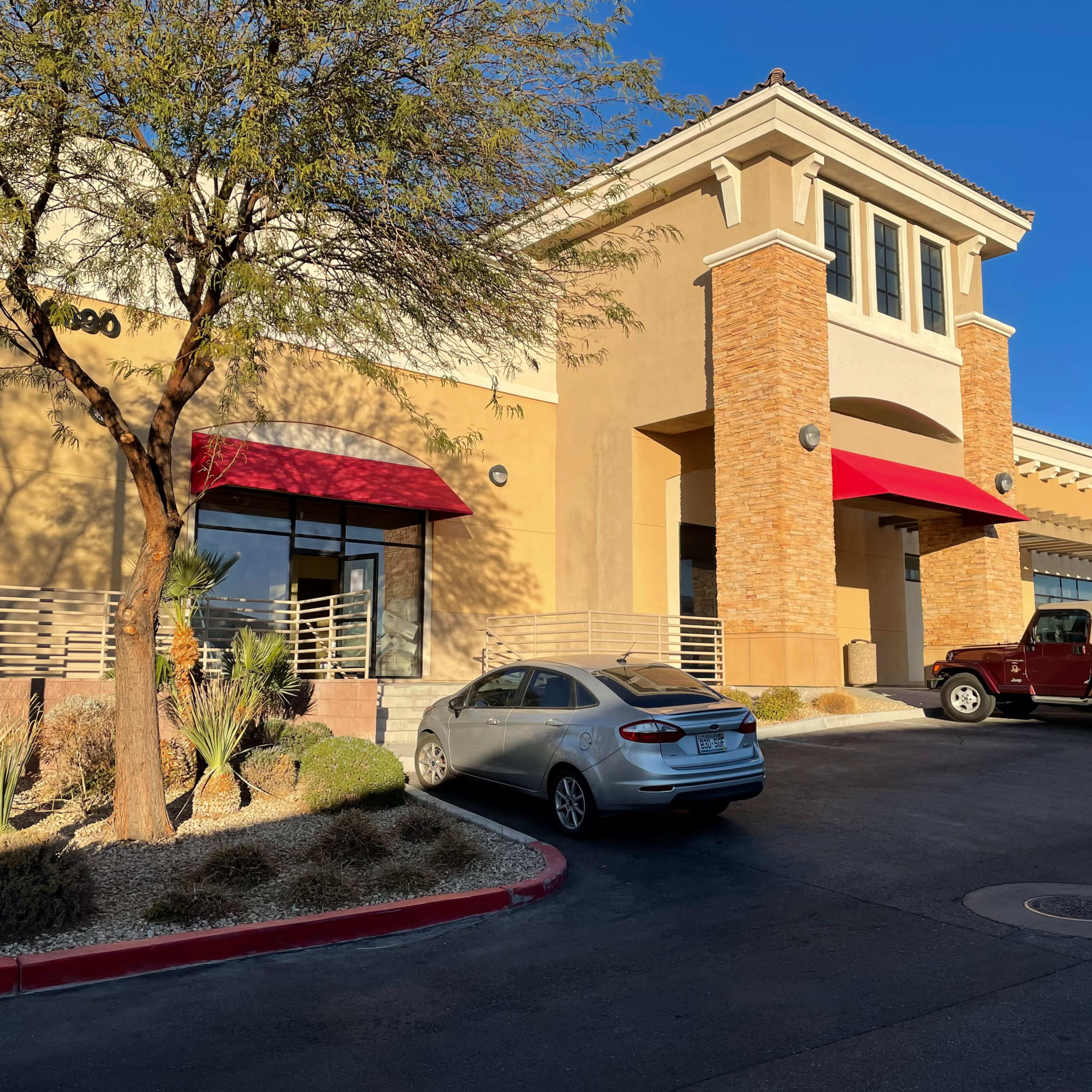 A commercial building with a stucco exterior, red awnings, and parked cars in front.