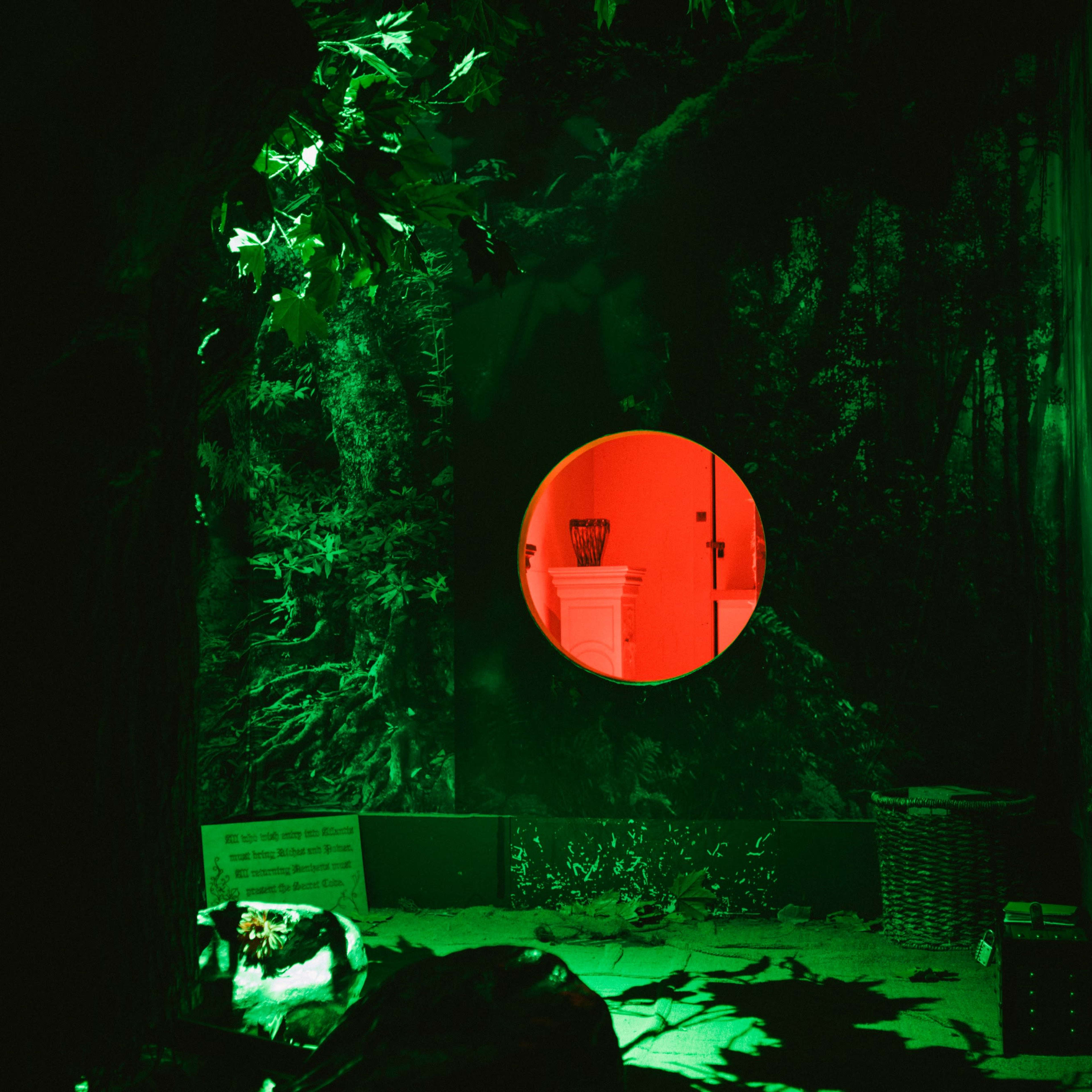 A dark, green-lit forest scene with a circular, red-lit opening revealing a white structure inside.